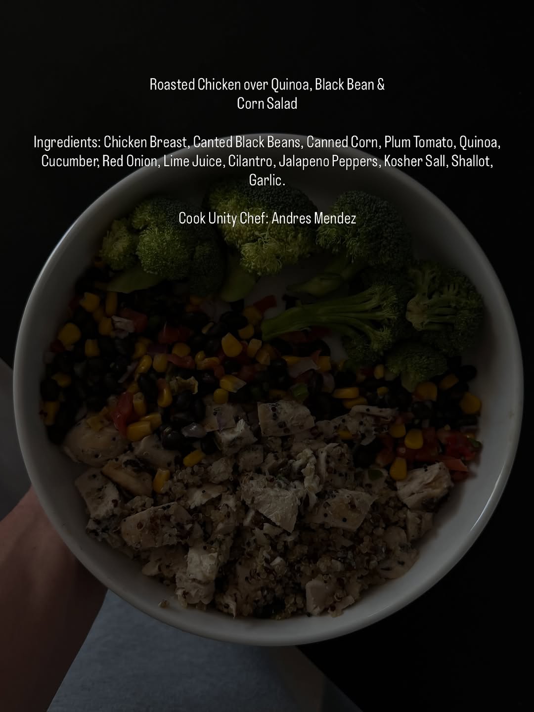 A bowl filled with roasted chicken over quinoa, black beans, corn salad, and assorted vegetables including broccoli and cucumber.