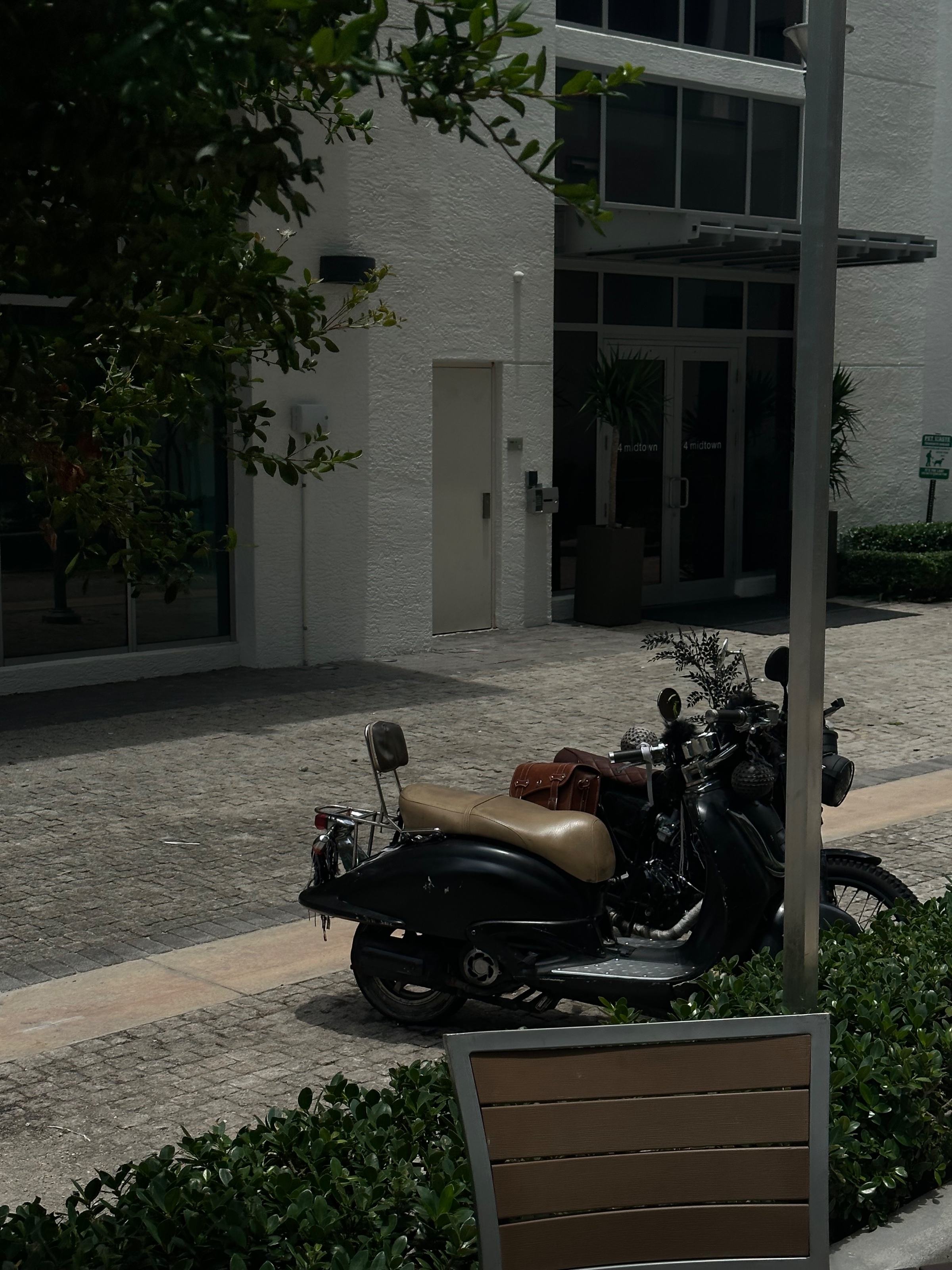 A vintage motorcycle parked in front of a modern building, surrounded by greenery.
