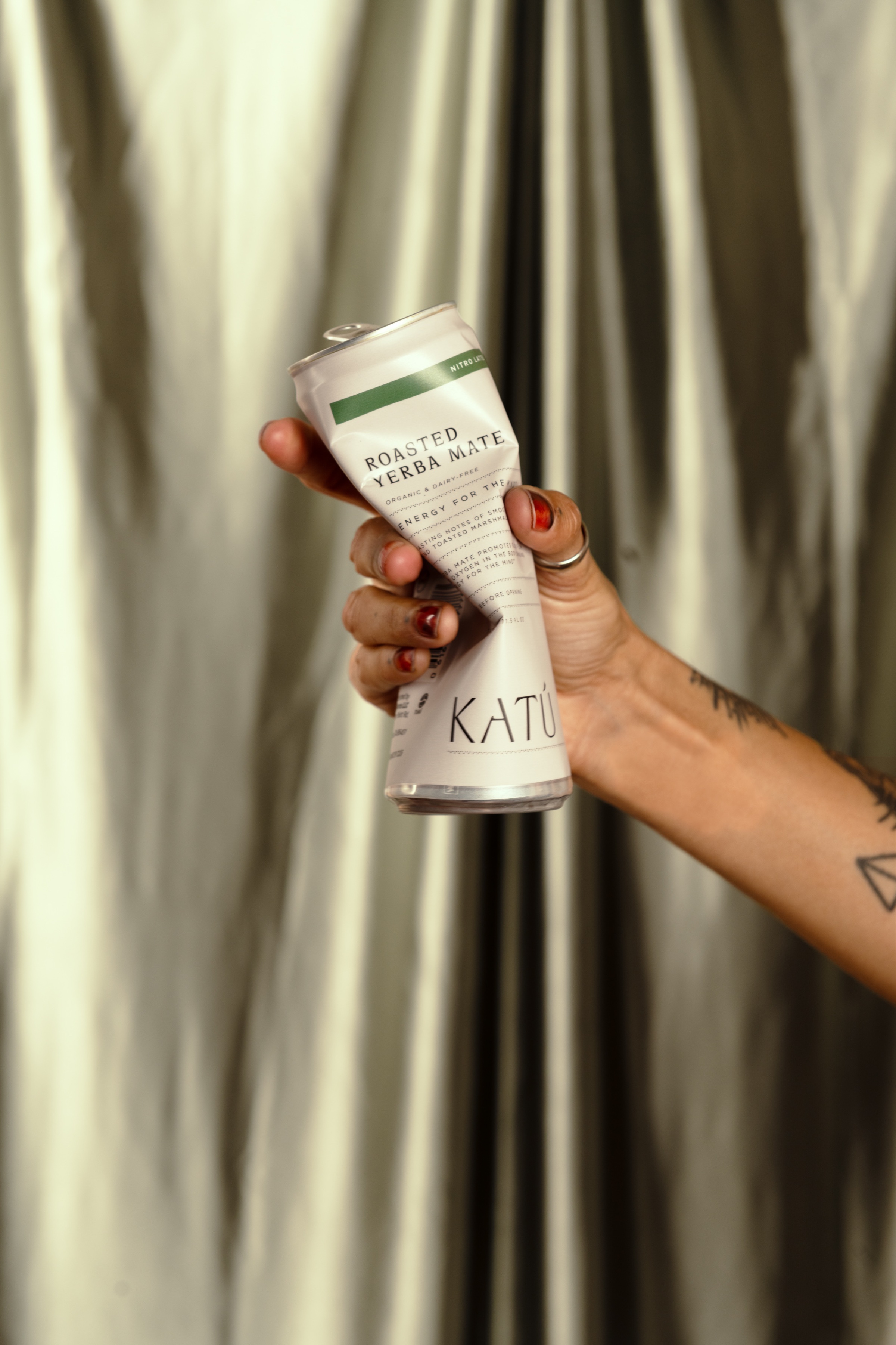 A hand holding a can of roasted green mate against a shimmering silver backdrop.