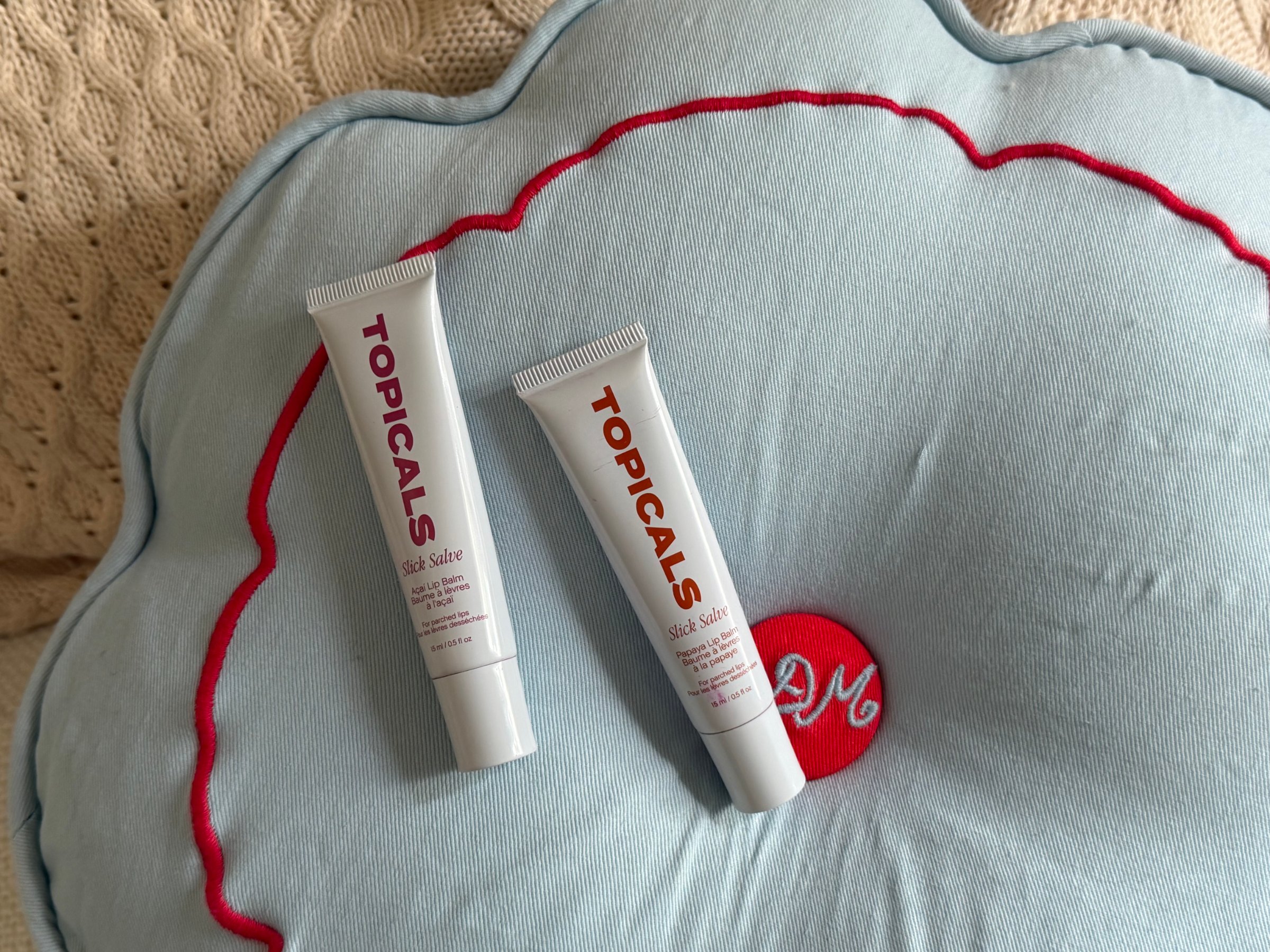Two tubes of Topicals skincare products placed on a light blue decorative pillow with red accents.