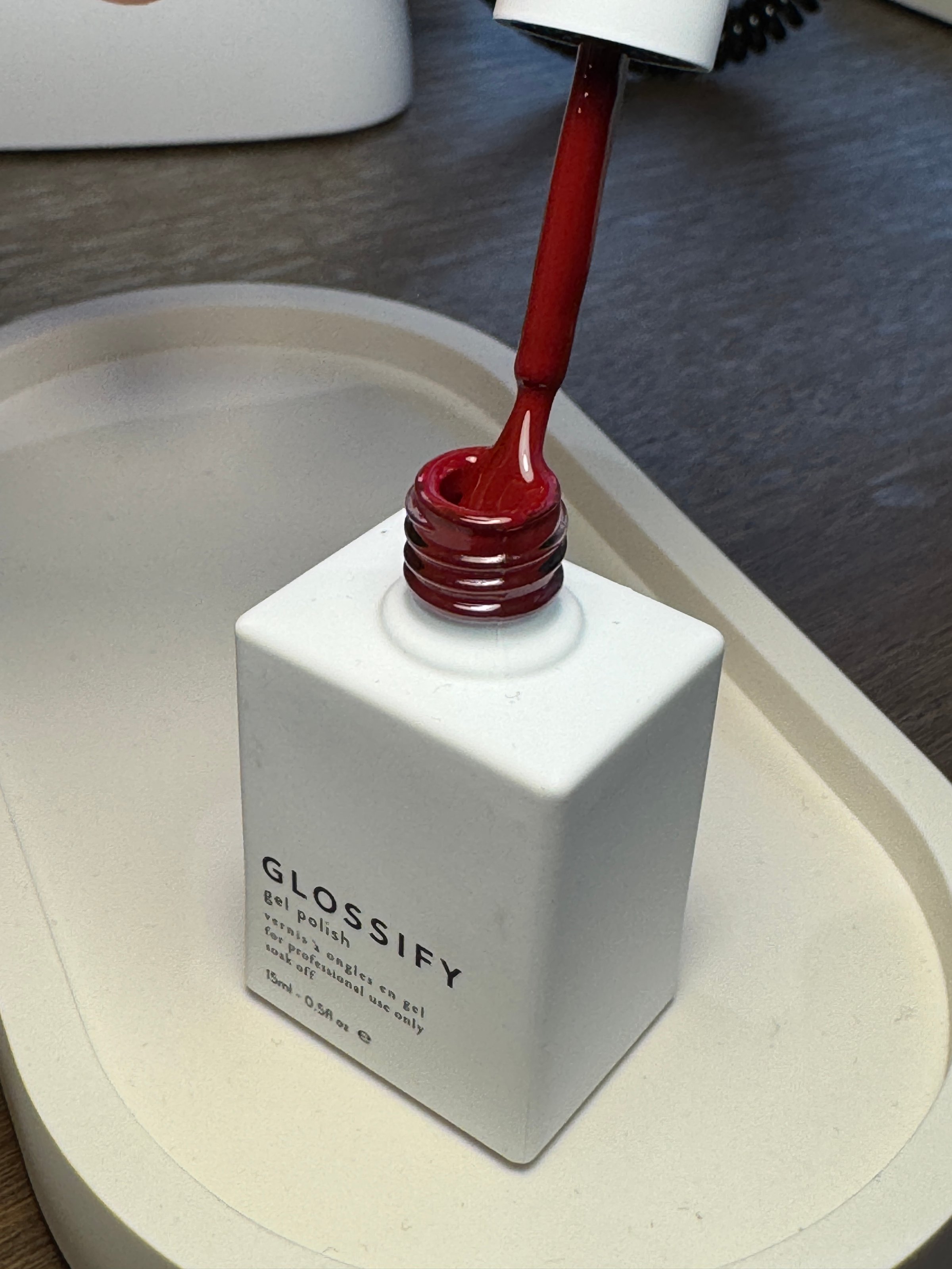 A bottle of red gel nail polish with a brush dipped in it, placed on a minimalist tray.