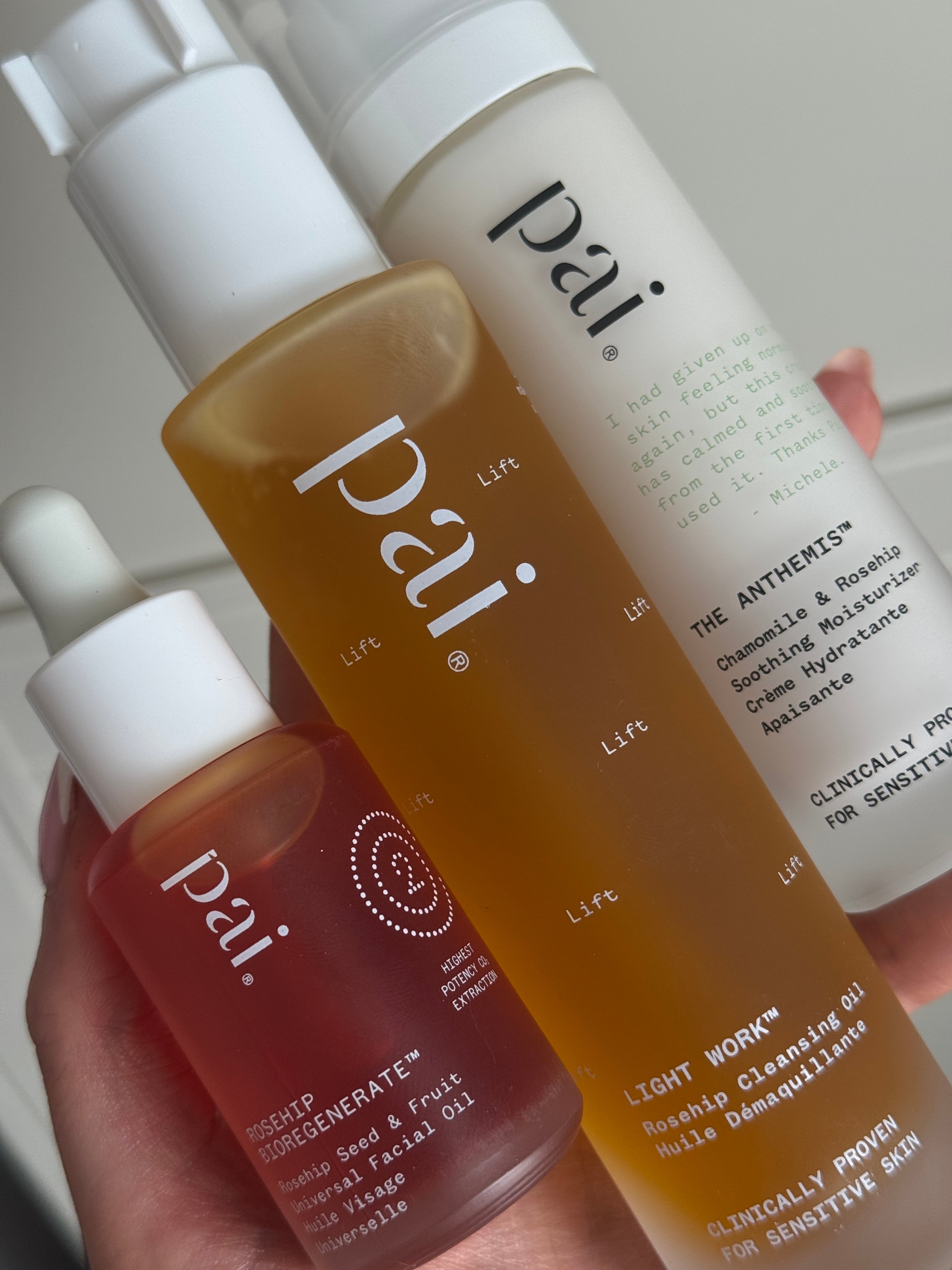 Three skincare products from the brand Pai, featuring a serum, cleansing oil, and moisturizer, held in a hand.