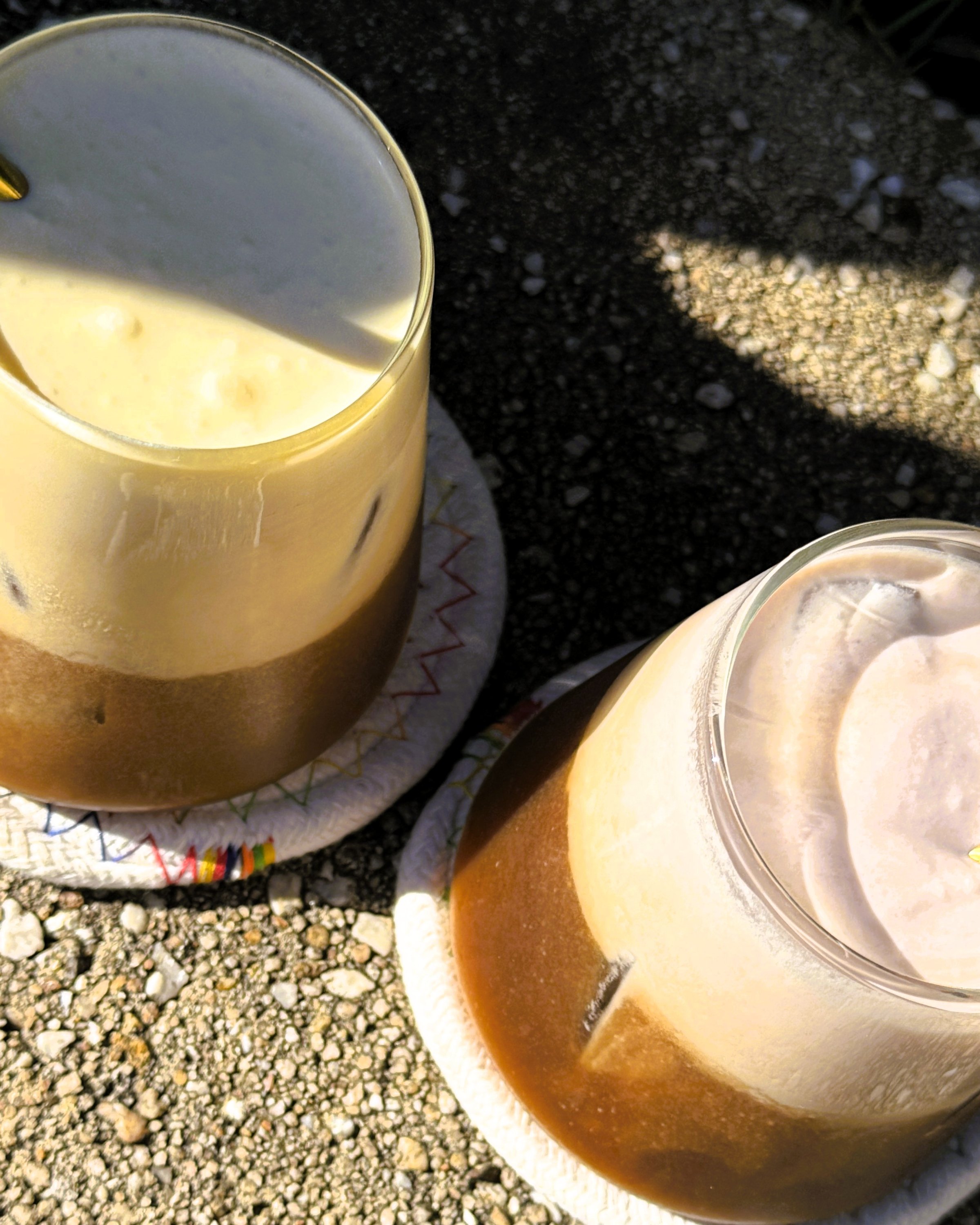 Two glasses of iced coffee with layered textures, sitting on a textured surface.