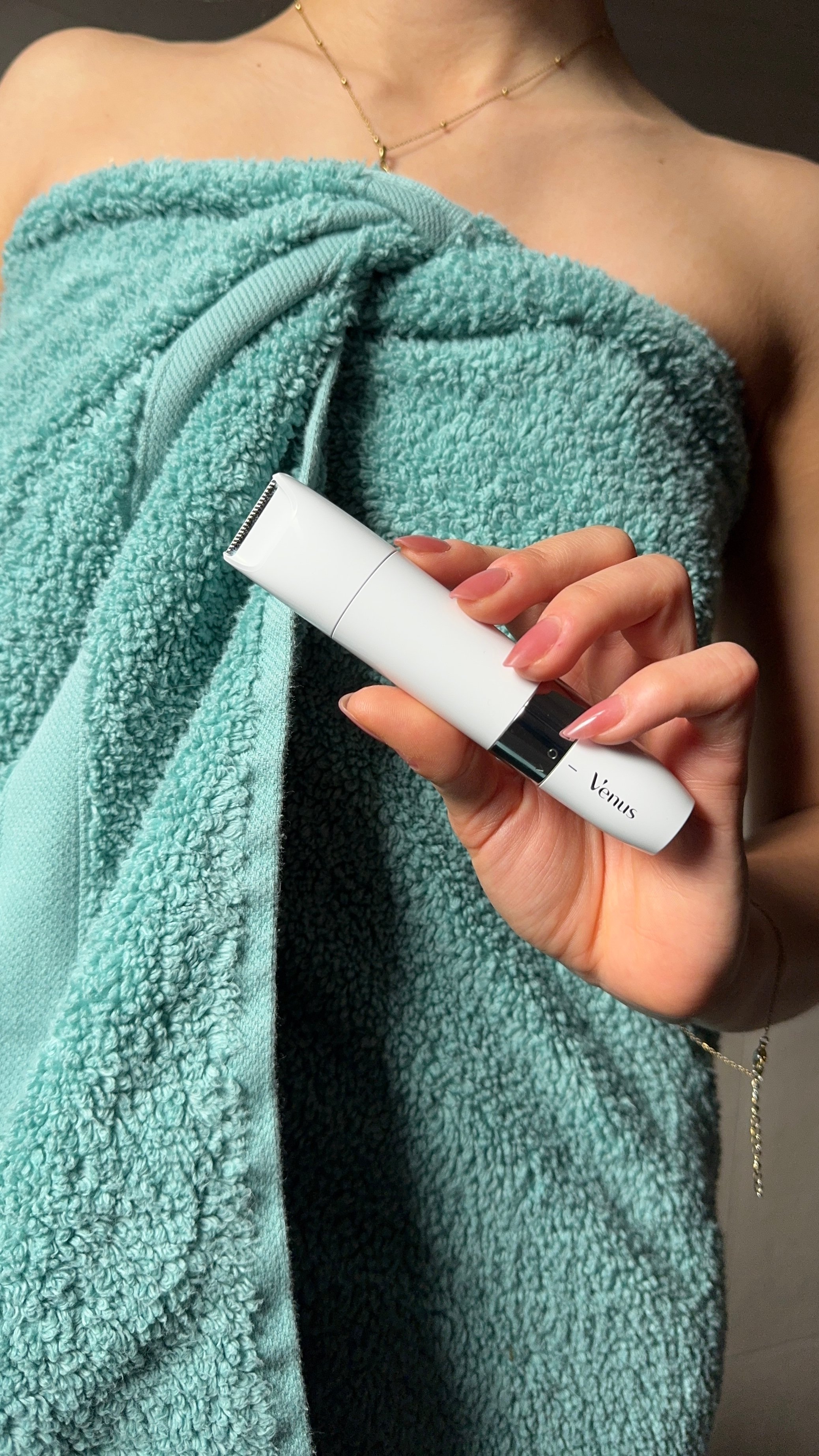 A person holding a sleek white beauty device while wrapped in a teal towel.