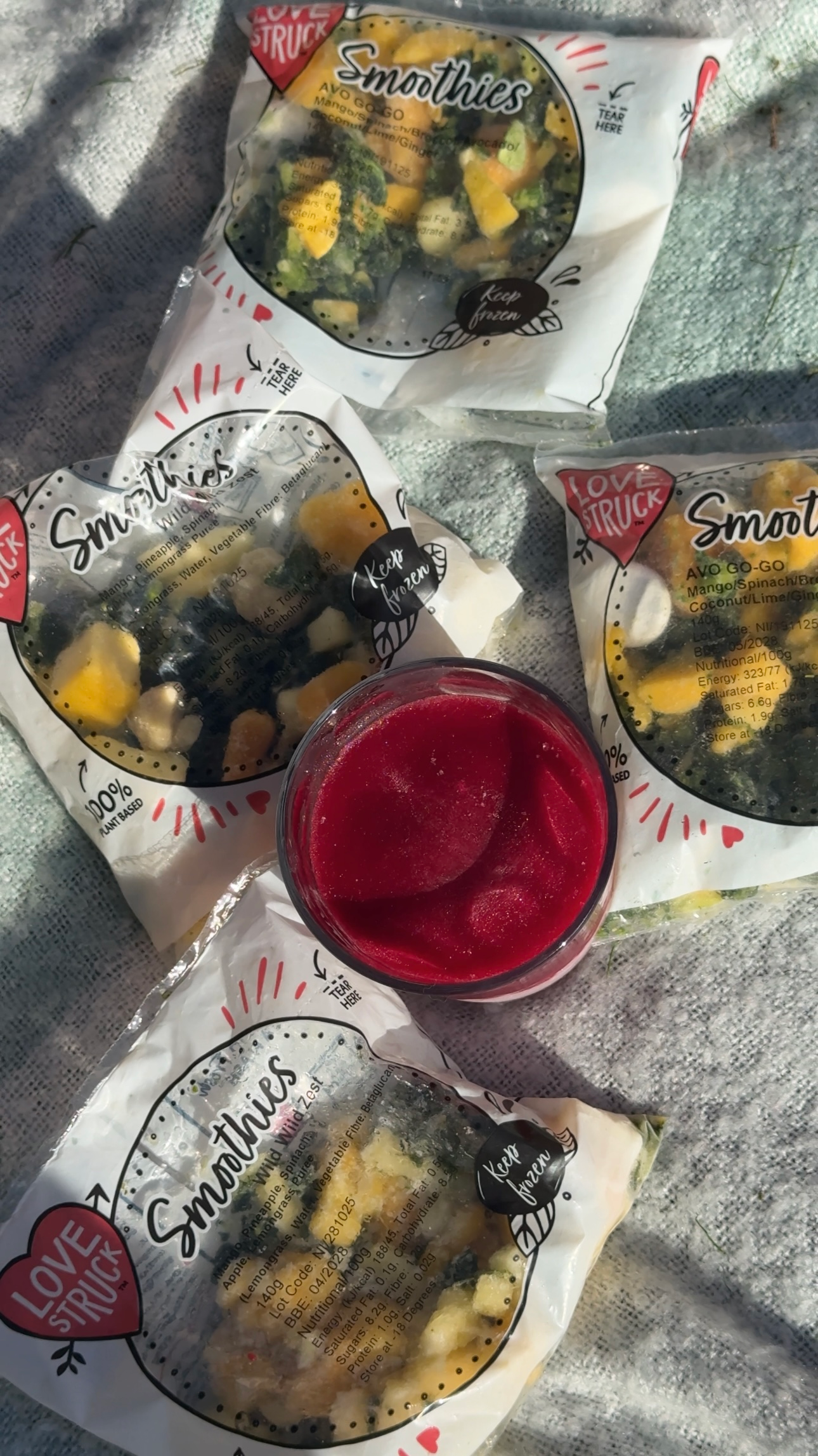 A collection of smoothie packs and a small bowl of vibrant red smoothie on a textured surface.