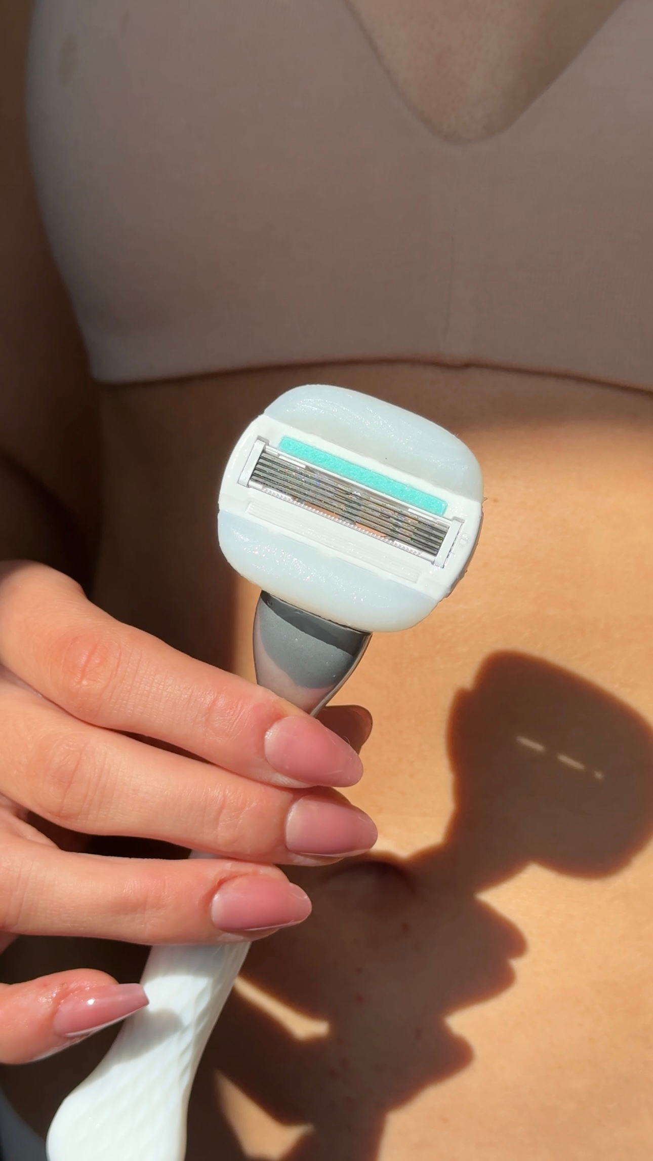 A close-up of a person holding a razor with a light blue handle, showcasing the blade and its design against a sunlit background.