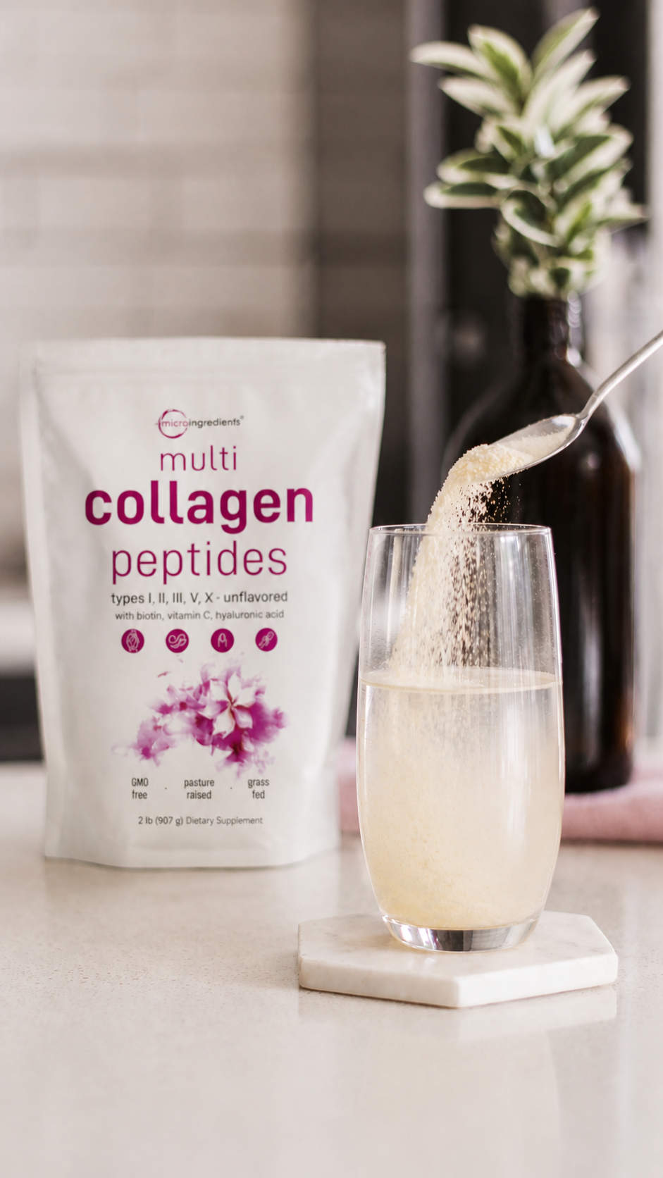 A glass of collagen peptide drink on a countertop, with a spoon pouring the powder from a bag labeled 'multi collagen peptides' in the background.
