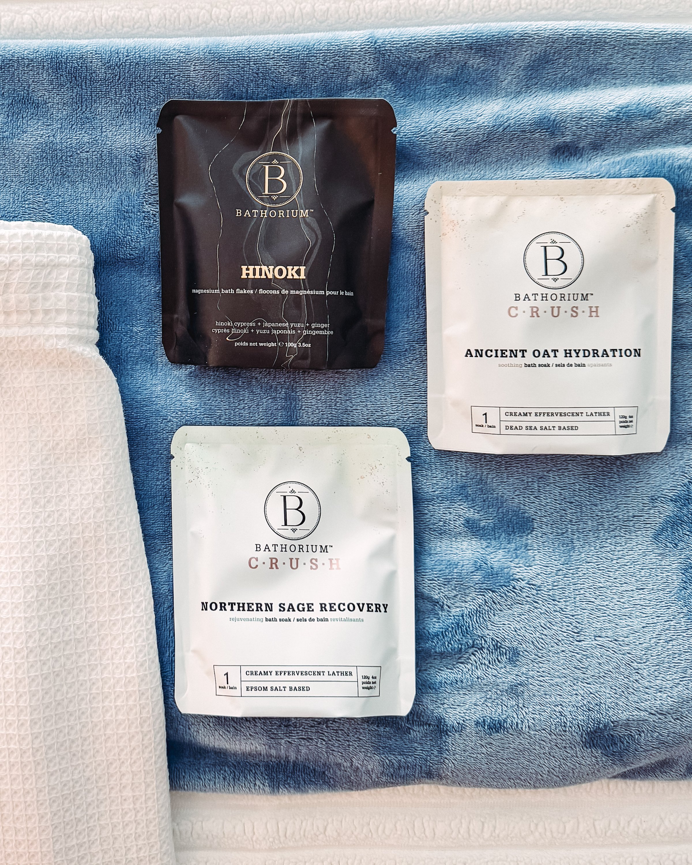 Three skincare product packets displayed on a soft blue towel, showcasing different formulations.