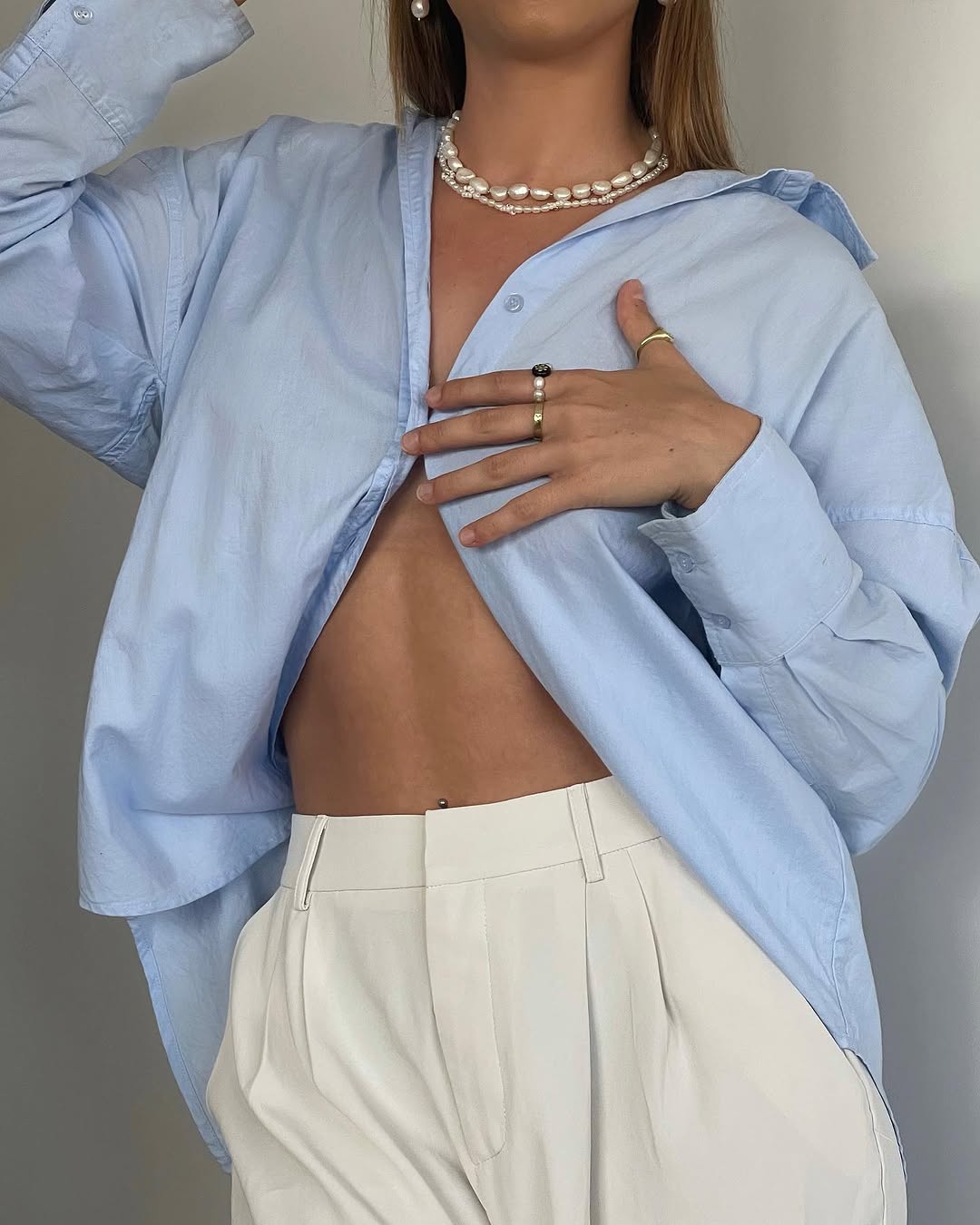 A person poses in a light blue oversized shirt and white trousers, showcasing a stylish and relaxed look.