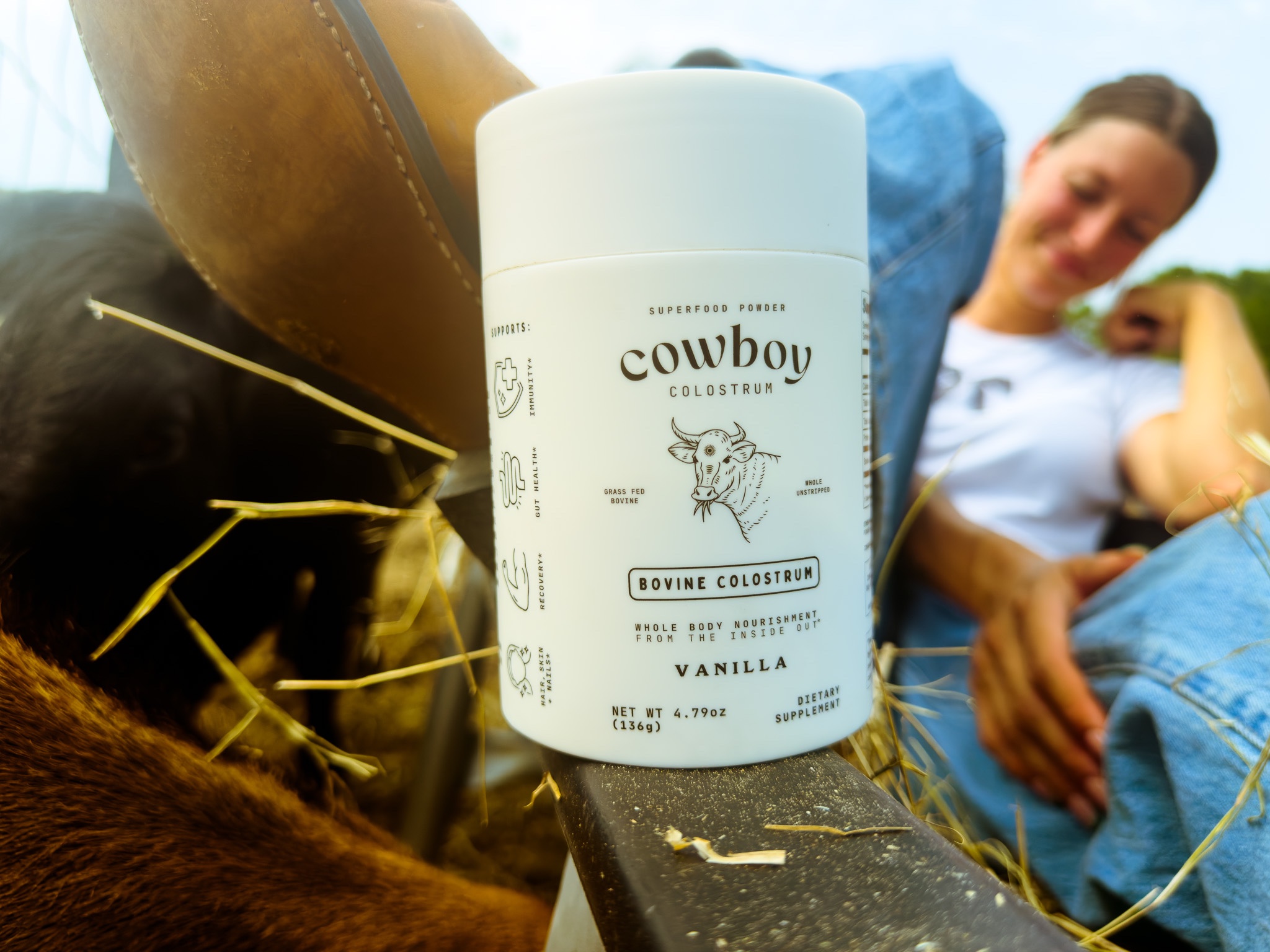 A close-up of a cowboy-themed body lotion container placed on a table with a blurred background of a person relaxing in a casual setting.