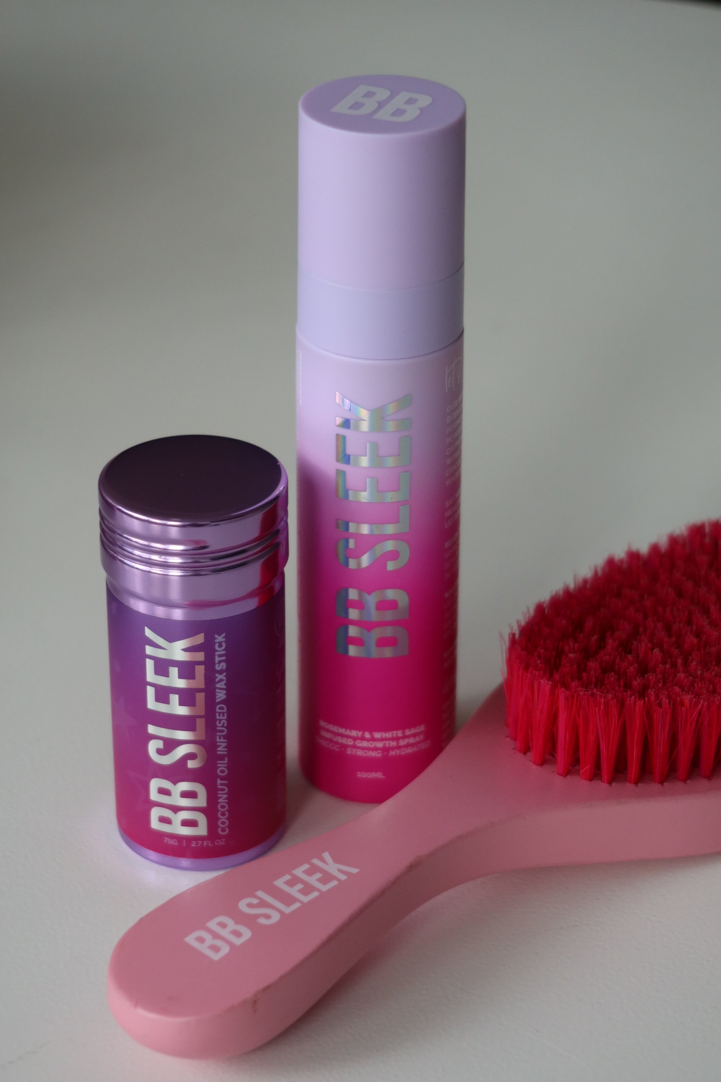A collection of BB Sleek beauty products including a purple container and a spray bottle, alongside a pink brush.