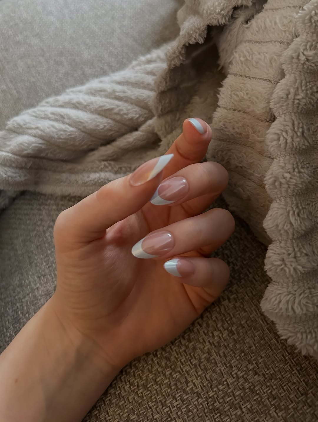 A close-up of a hand displaying a stylish manicure with light pink and white tips, resting on a textured fabric surface.