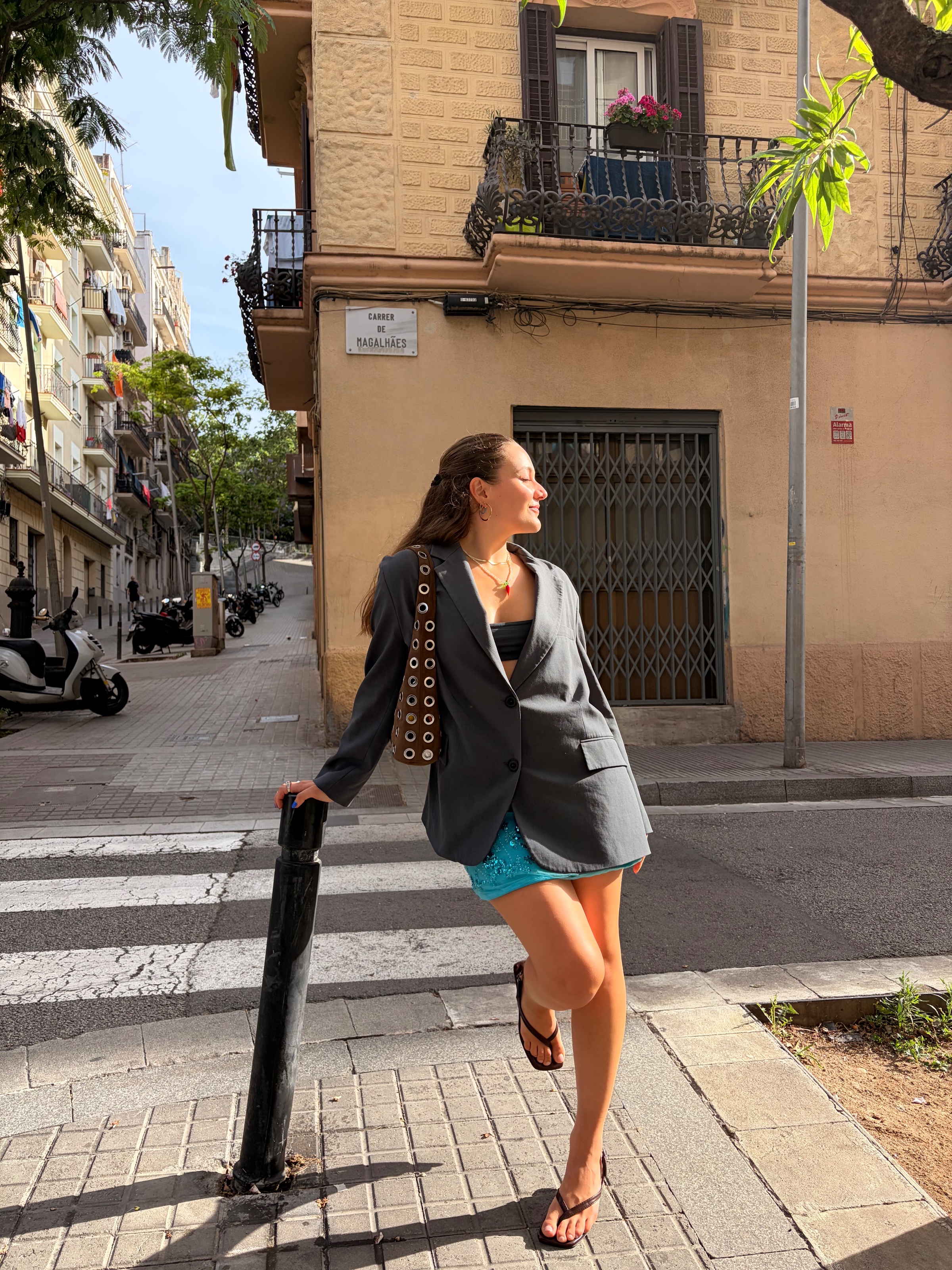 A woman stands confidently on a city street, wearing a stylish oversized blazer and a short skirt, with a playful pose against a lamppost.
