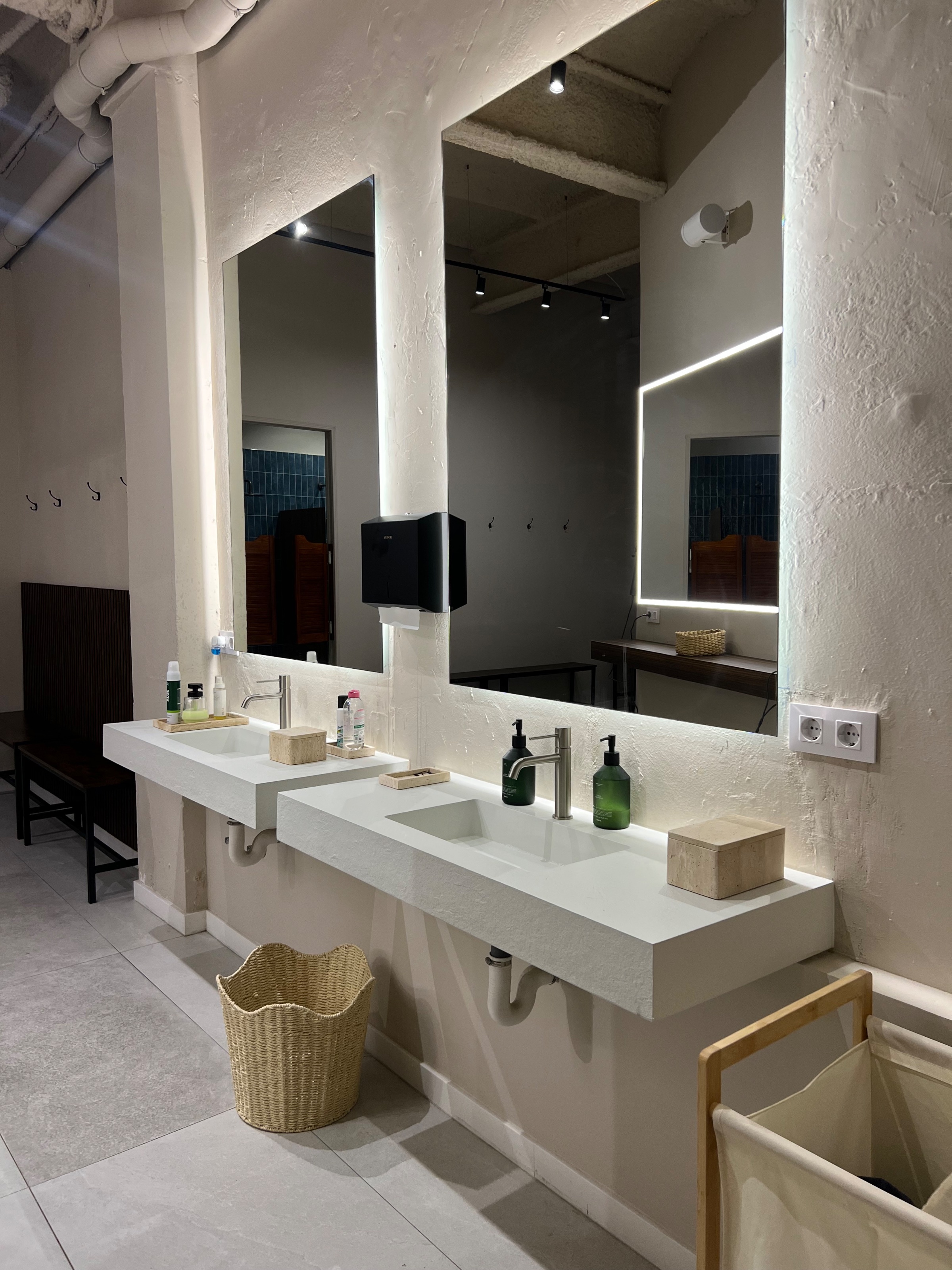 A modern bathroom with two sinks, illuminated mirrors, and minimalist decor. Natural light enhances the clean aesthetic of the space.