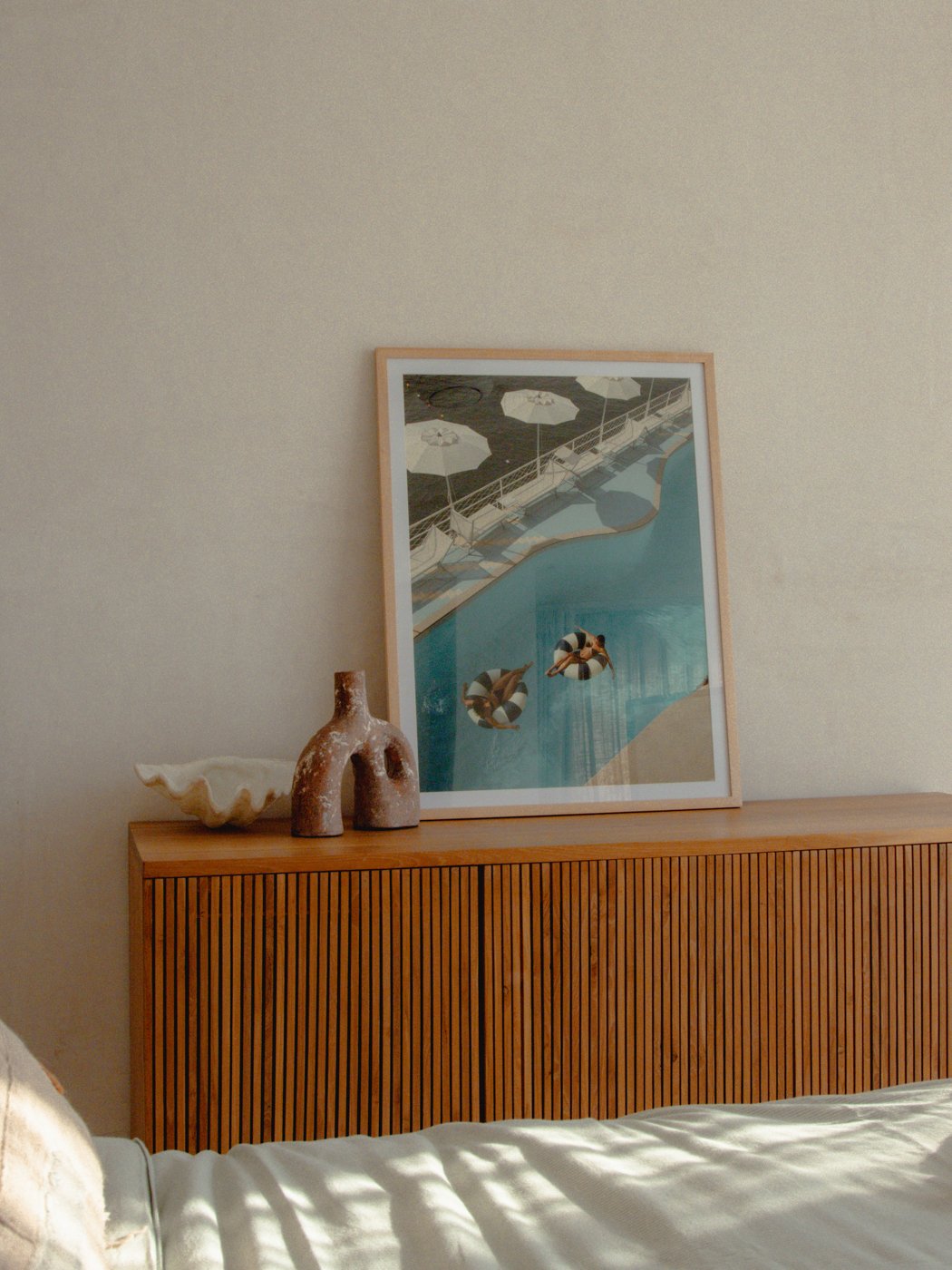 A serene interior scene featuring a wooden sideboard with a decorative vase and a shell, alongside a framed artwork depicting a beach view.