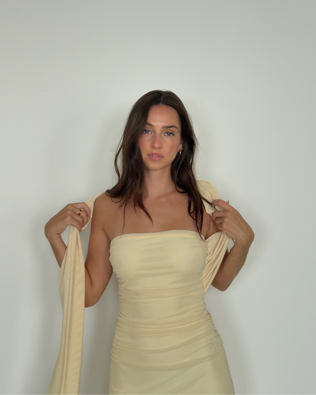 A woman in a strapless beige dress holds a matching wrap, posing against a plain background.