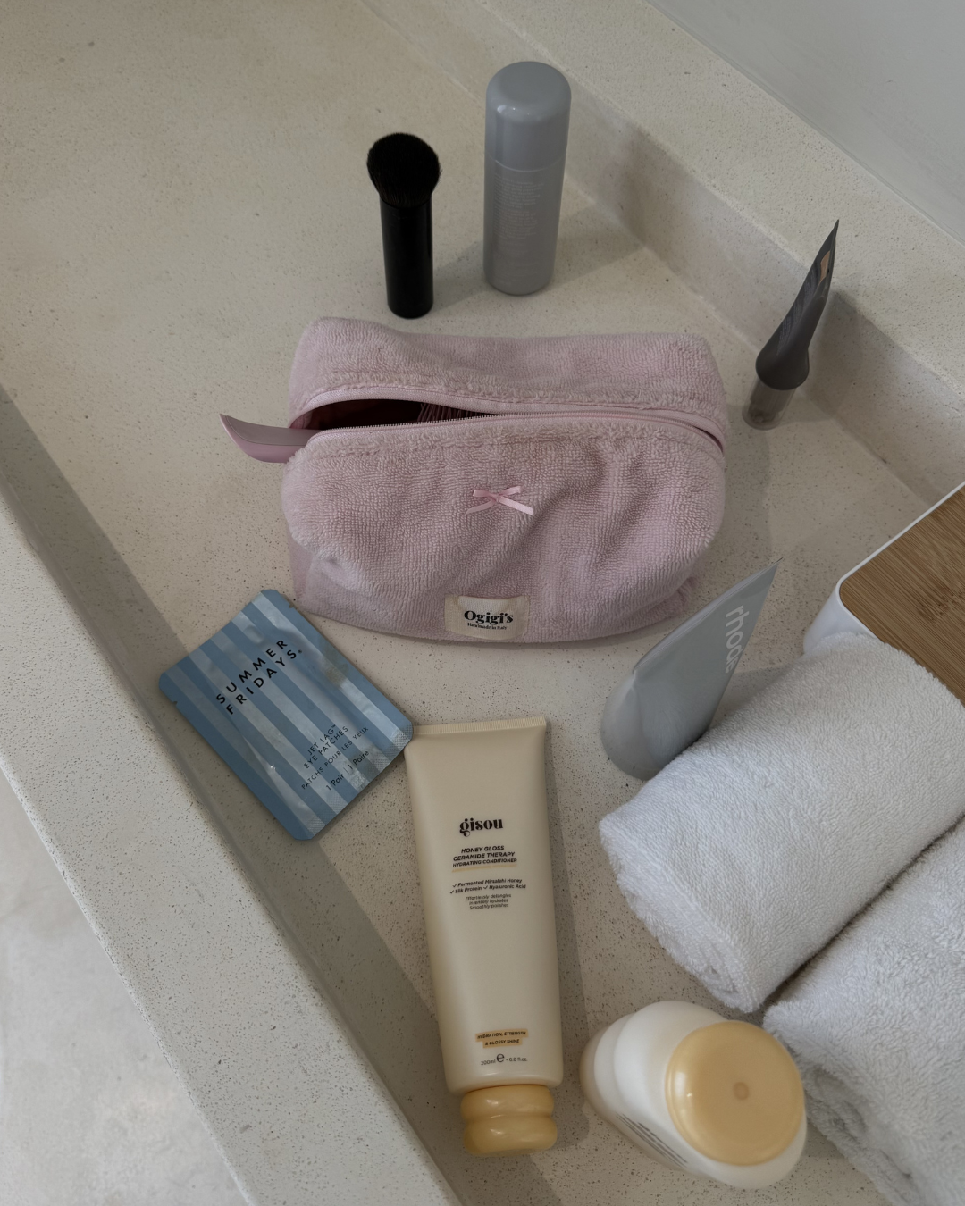 A neatly arranged collection of skincare products and tools on a countertop, including a pink pouch, a facial brush, and various tubes and bottles.