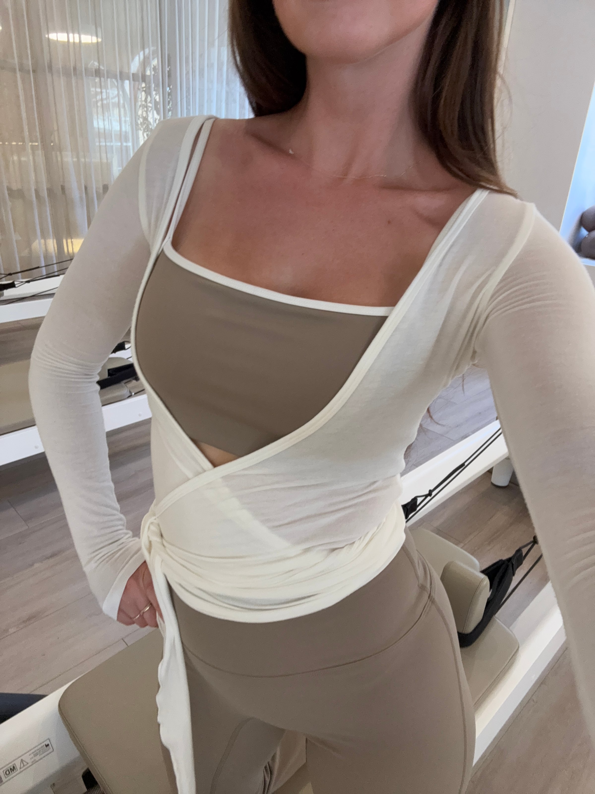 A person wearing a stylish beige workout outfit with a wrap top, posing confidently in a bright, modern studio.