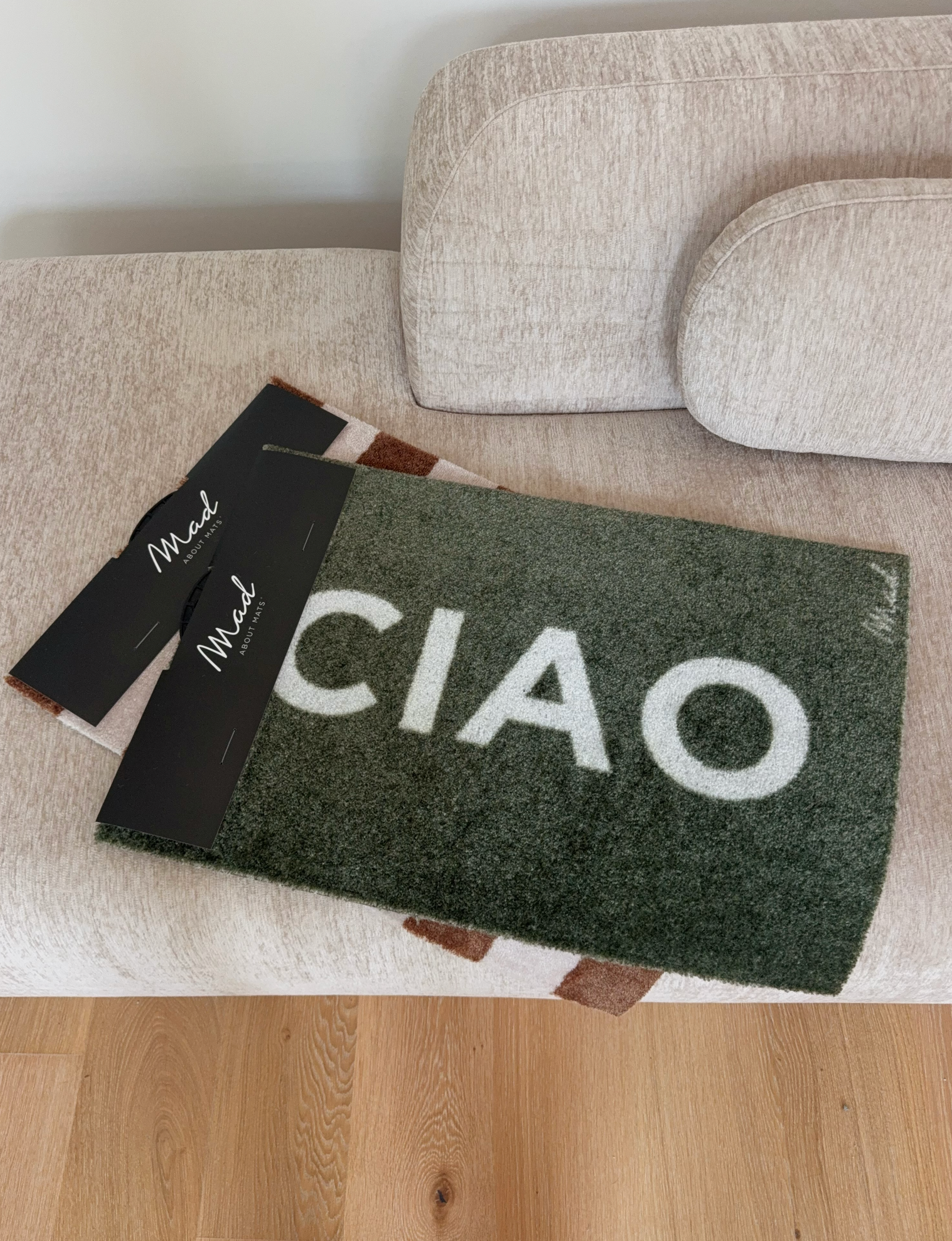 A green doormat with the word 'CIAO' printed in white, placed on a light-colored sofa.