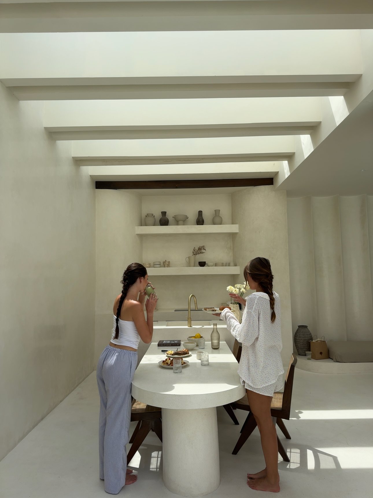Two women enjoying a meal at a modern, minimalist dining table in a bright, airy space.