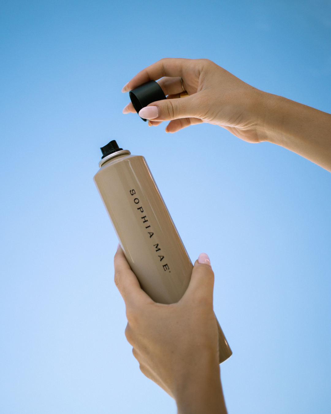 A person's hands holding a stylish water bottle with the brand name 'SOPHIA MAE' visible, against a clear blue sky.
