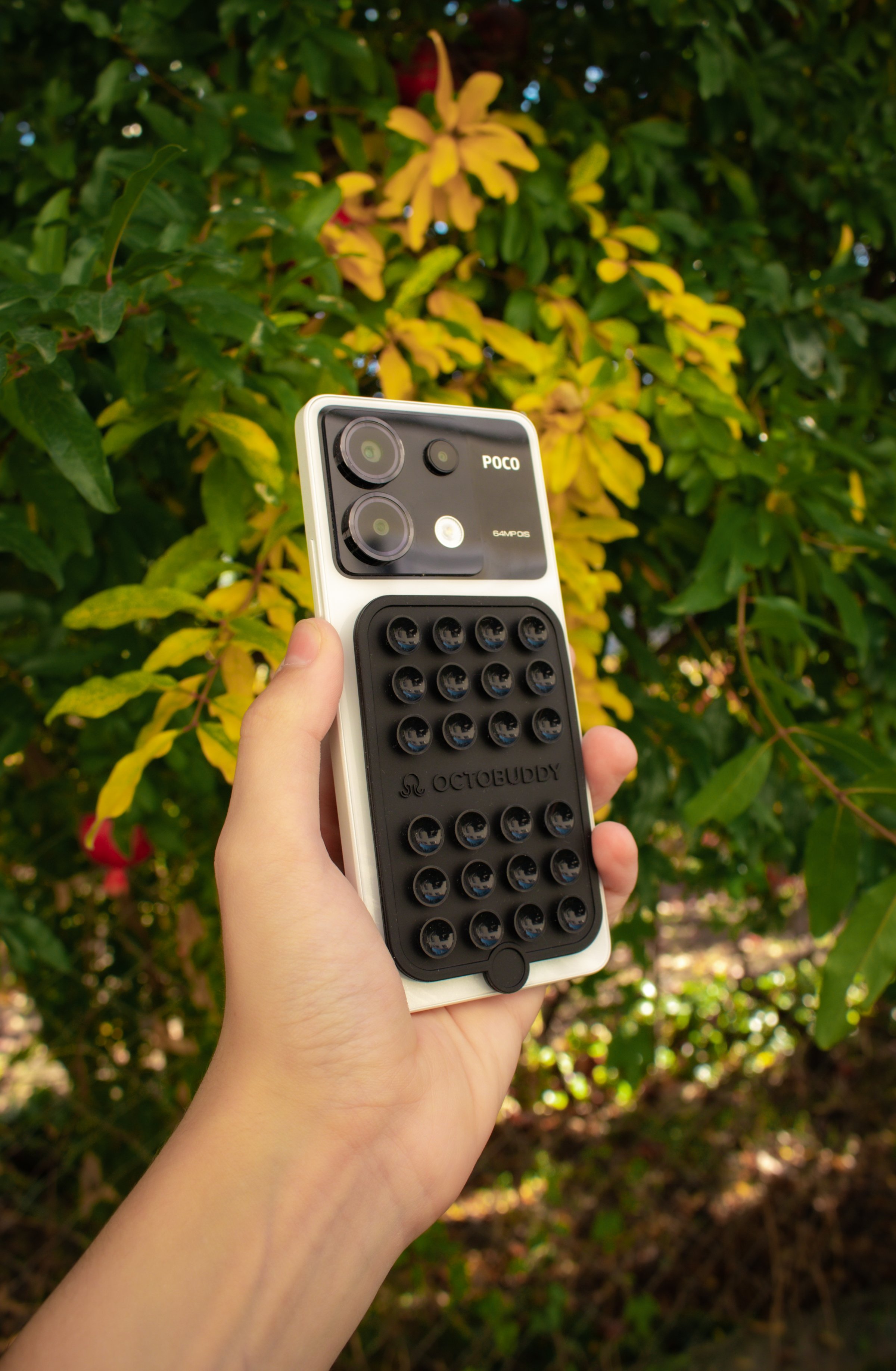 A hand holding a smartphone with a unique textured case against a backdrop of vibrant green foliage.
