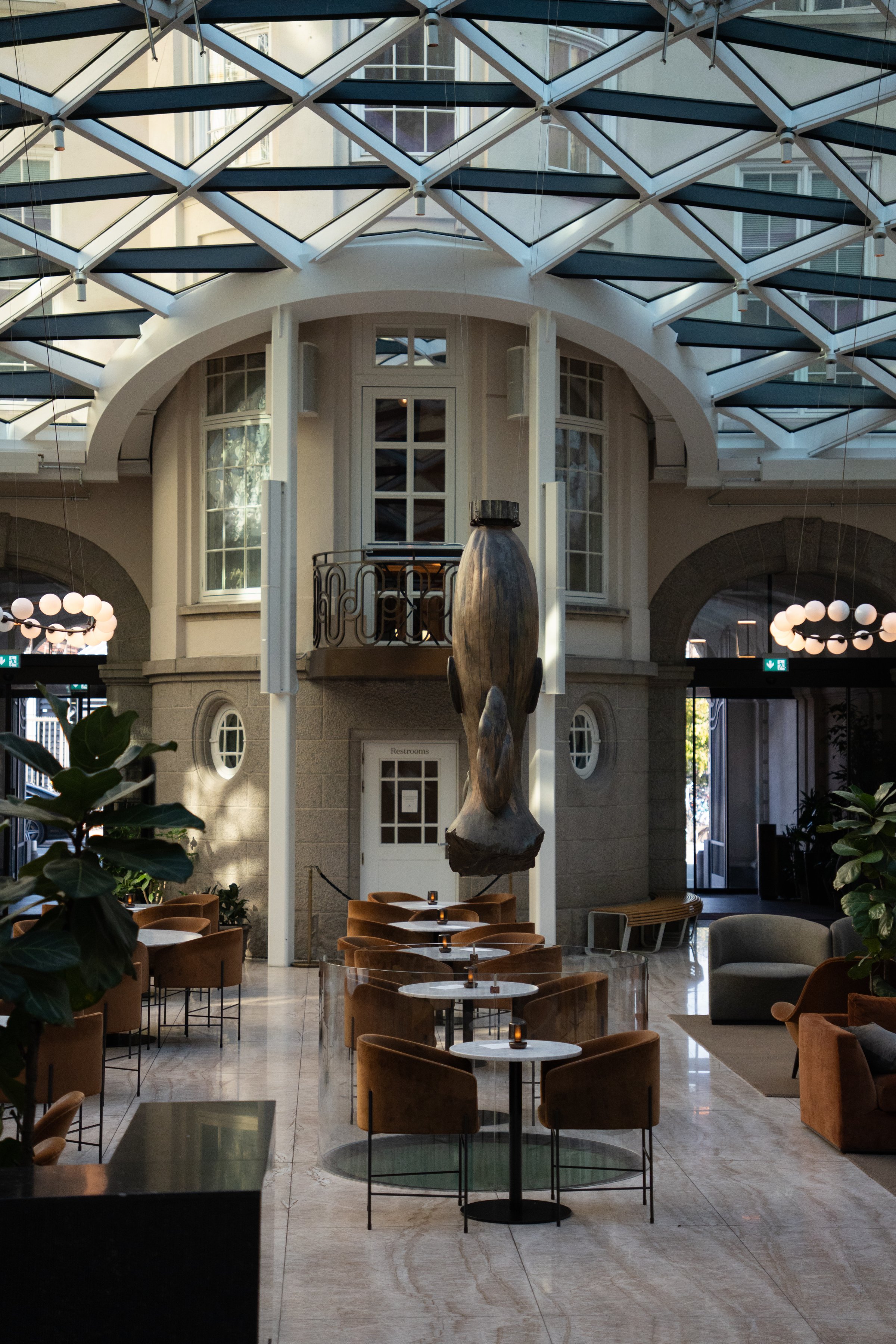 A stylish interior of a modern café featuring elegant seating arrangements and a large sculpture suspended from the ceiling.