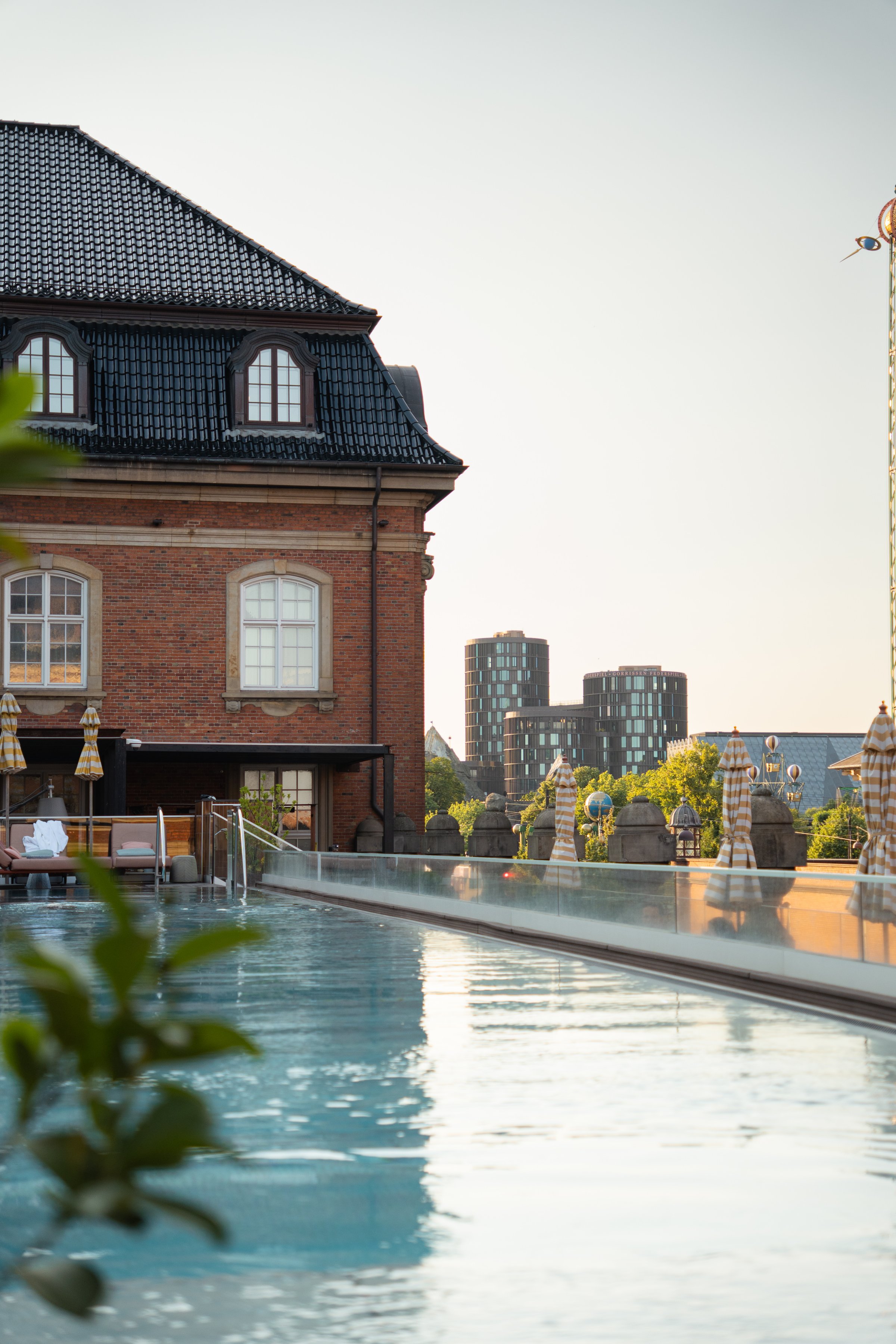 A serene poolside view featuring a historic brick building and modern architecture in the background, surrounded by greenery.