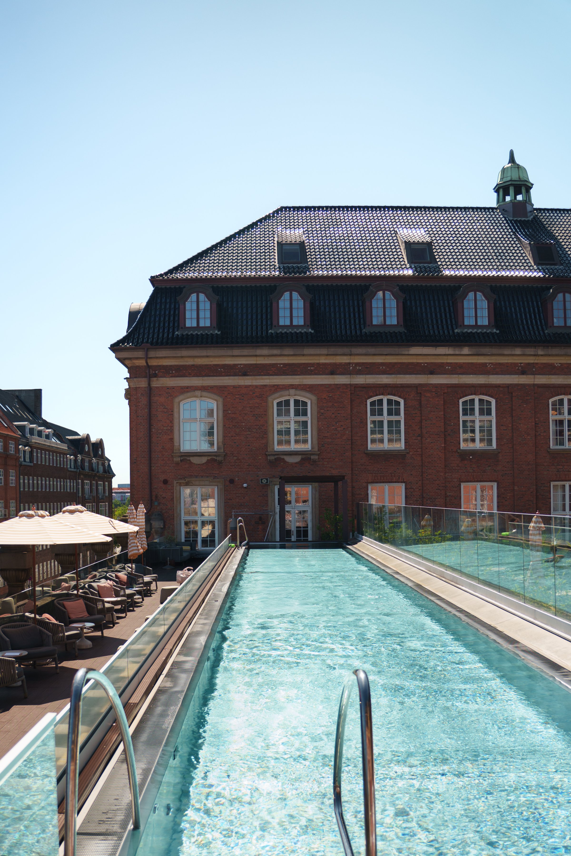 A luxurious swimming pool with clear water, leading towards a historic brick building under a clear blue sky.