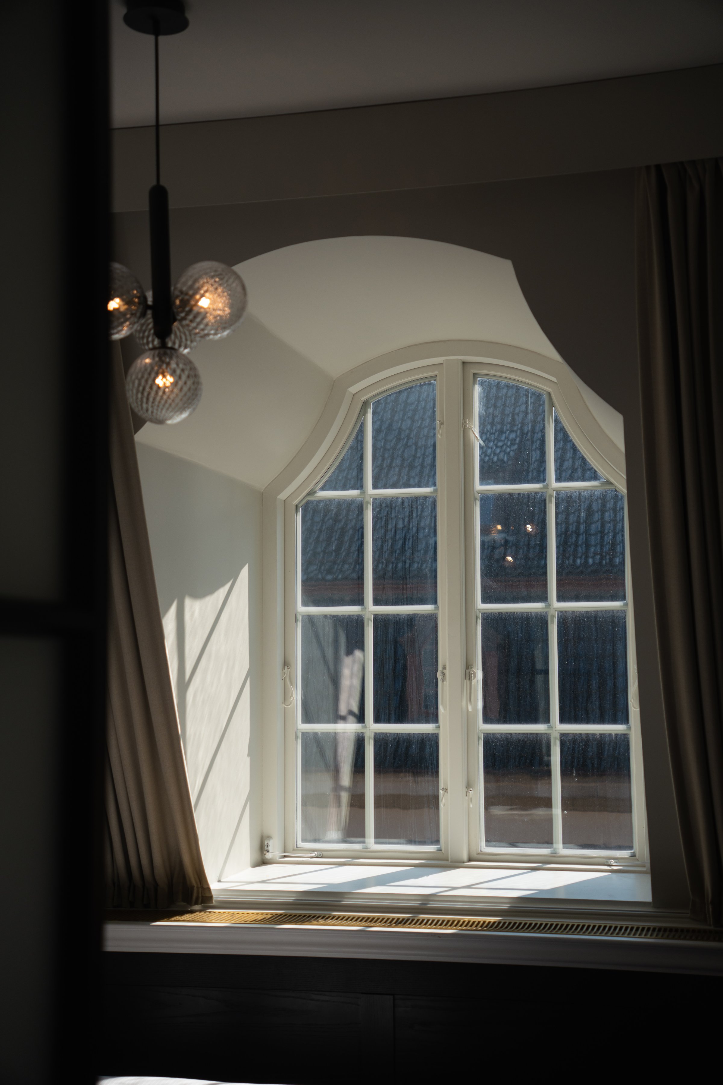 A well-lit window with multiple panes, framed by elegant curtains, casting shadows on a surface below.