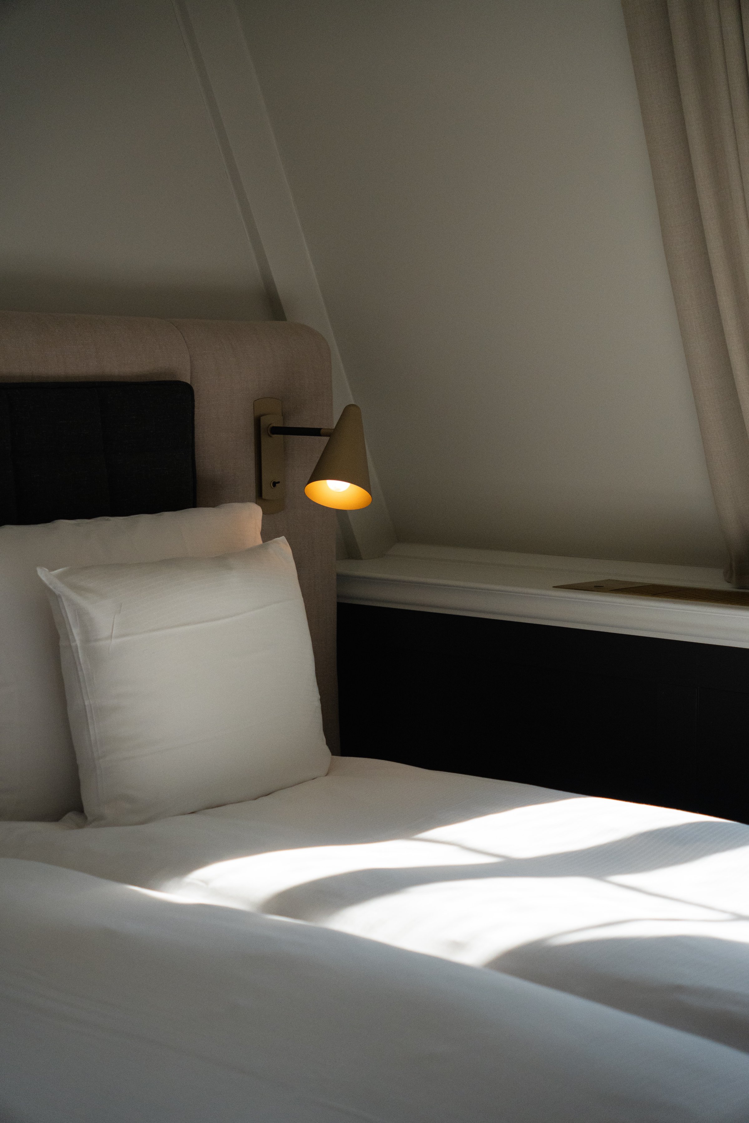 A cozy hotel room featuring a neatly made bed with white pillows and a lamp casting soft light, creating a warm atmosphere.