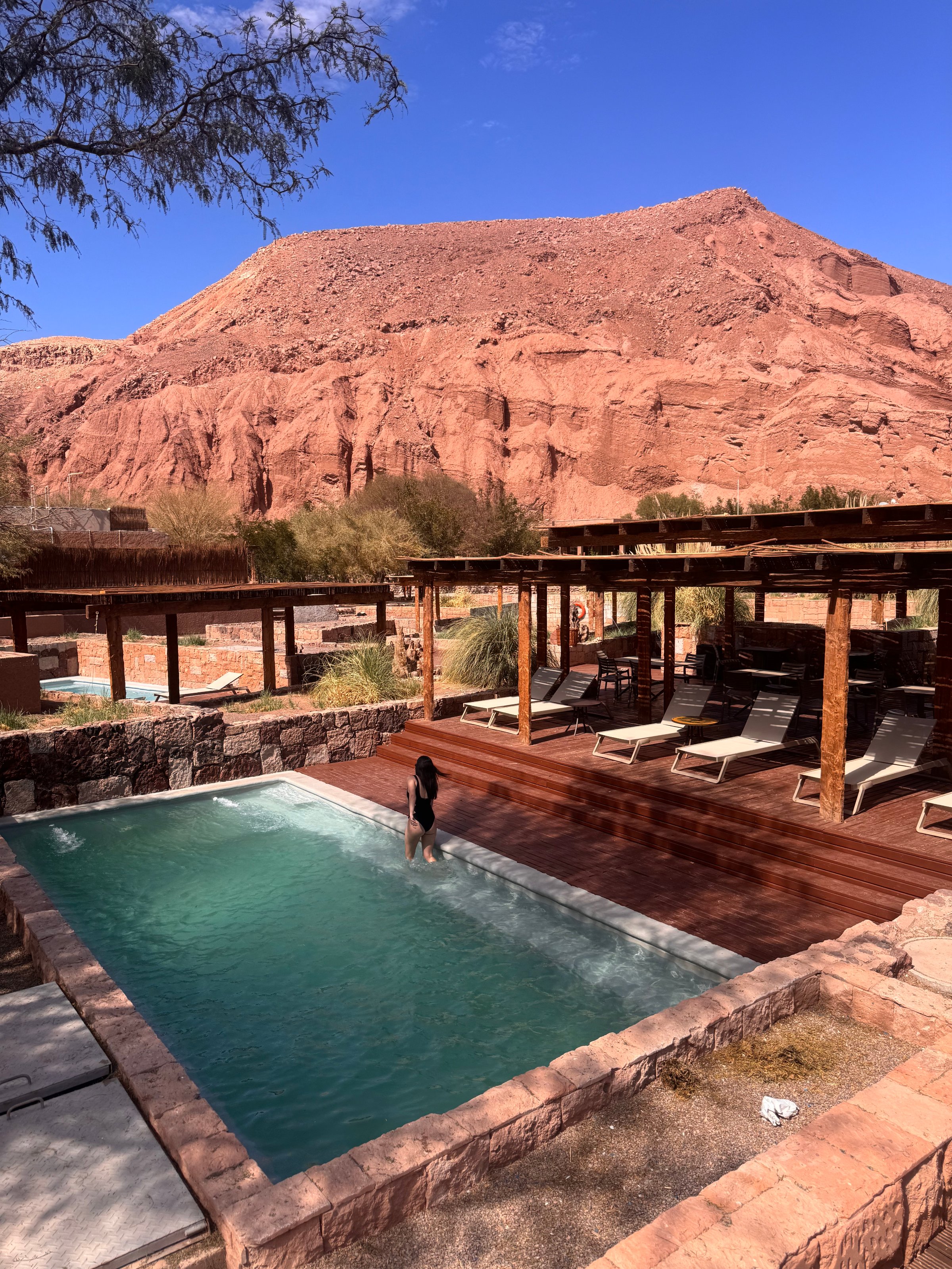 A serene pool surrounded by rustic wooden structures and natural rock formations under a clear blue sky.