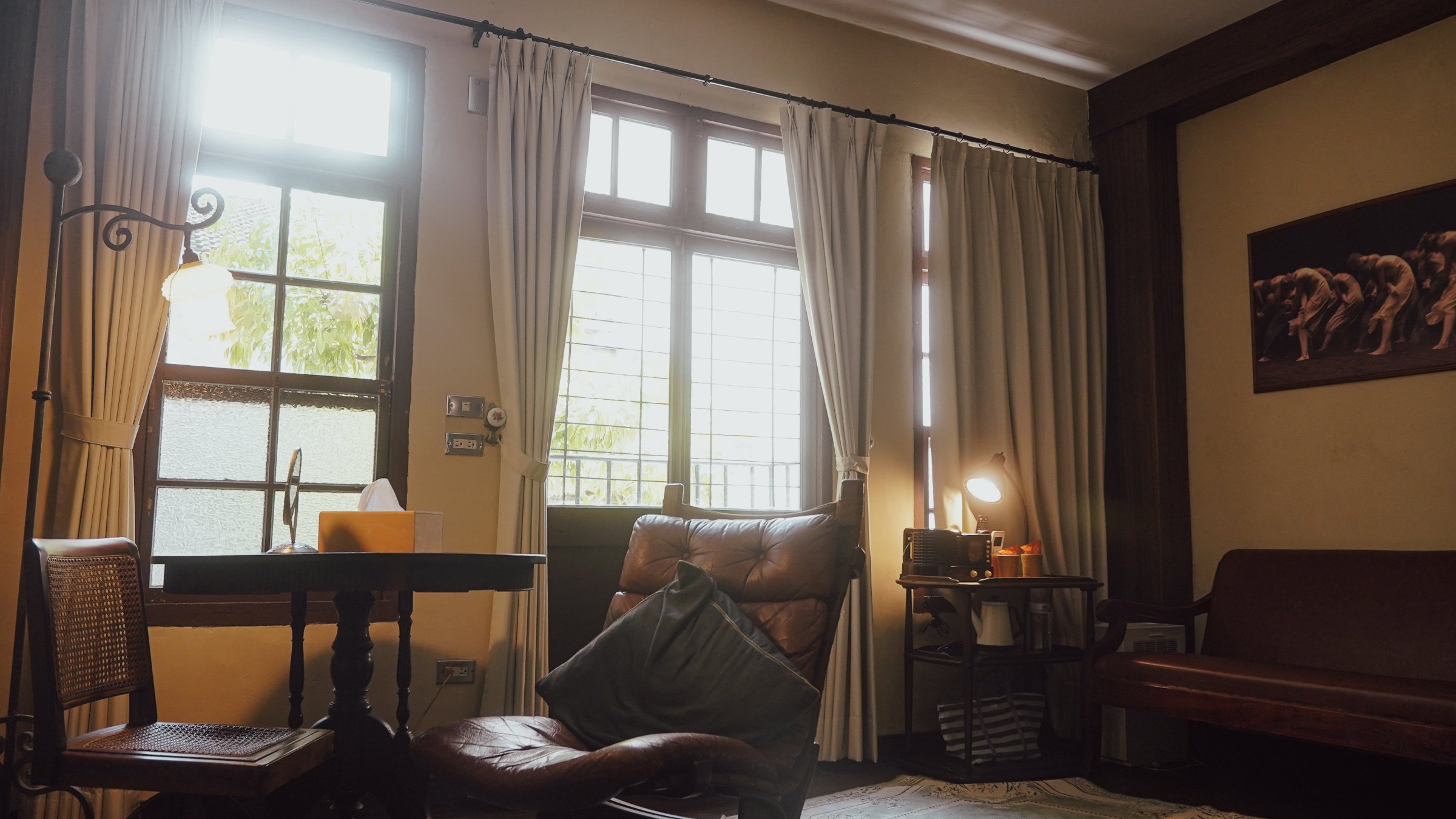 A cozy interior space featuring a wooden table, leather chairs, and large windows with curtains, creating a warm atmosphere.