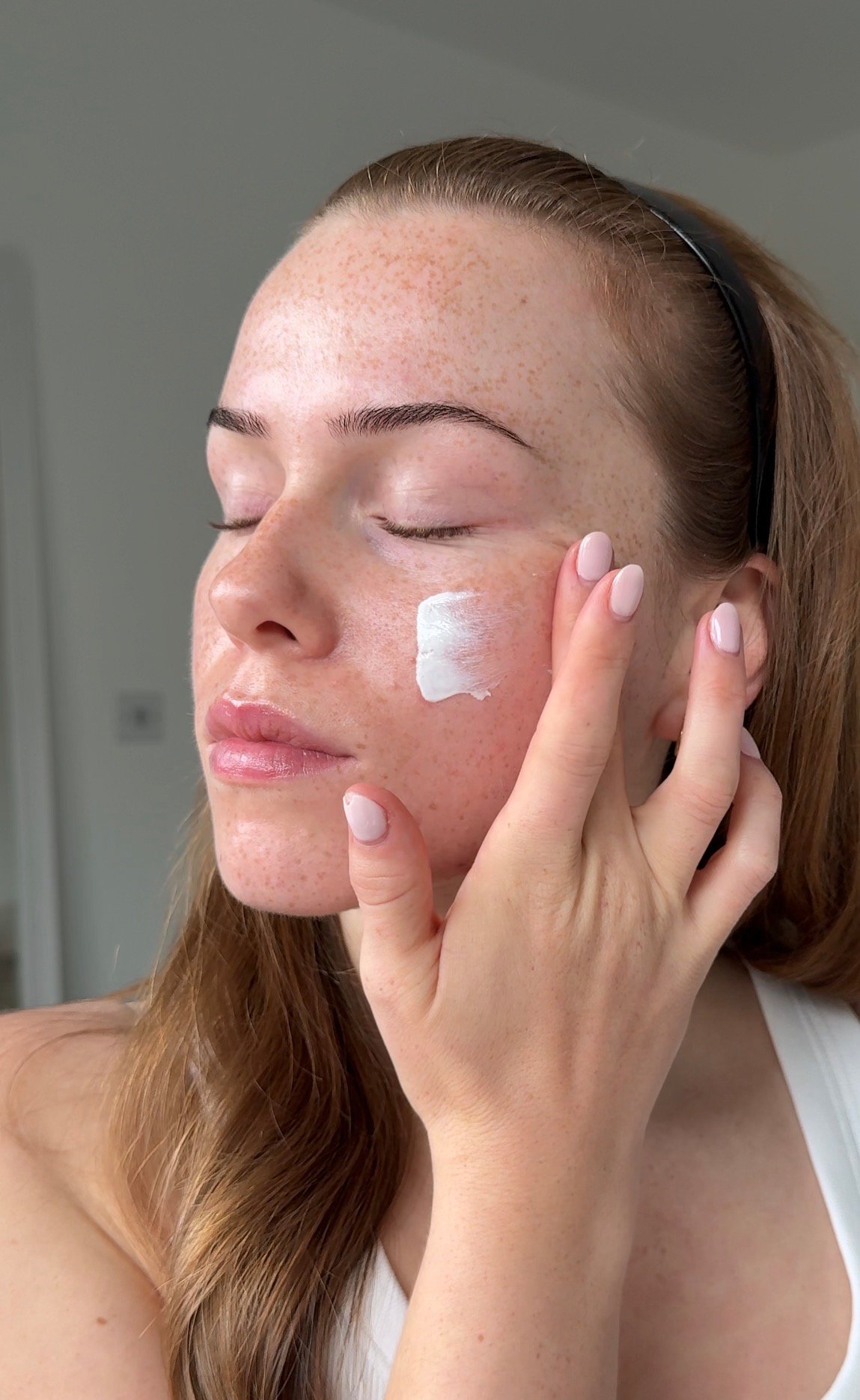 A person applying skincare cream to their face, showcasing a natural beauty look with a focus on skincare routine.