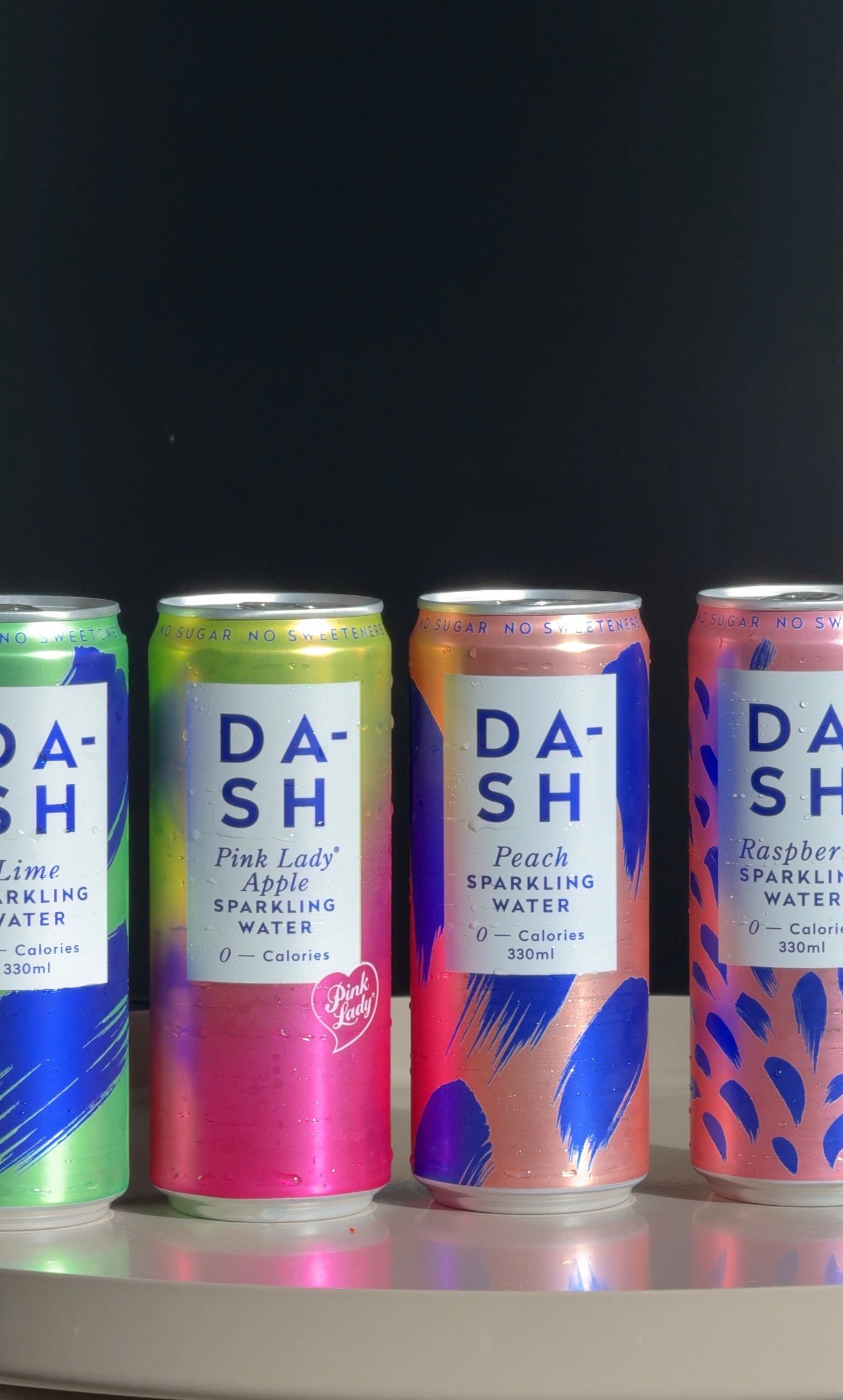 Four colorful cans of DASH sparkling water in various flavors displayed on a table.