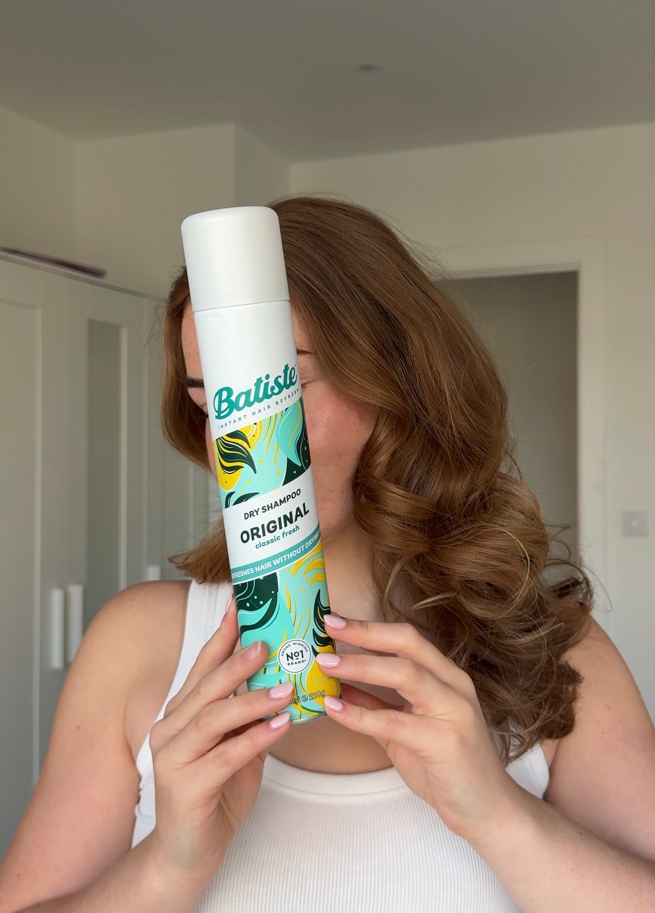 A person holding a can of Batiste dry shampoo in front of their face, showcasing the product's vibrant packaging.