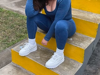 A person sitting on yellow steps, wearing a blue athletic outfit and white sneakers, with a relaxed pose.