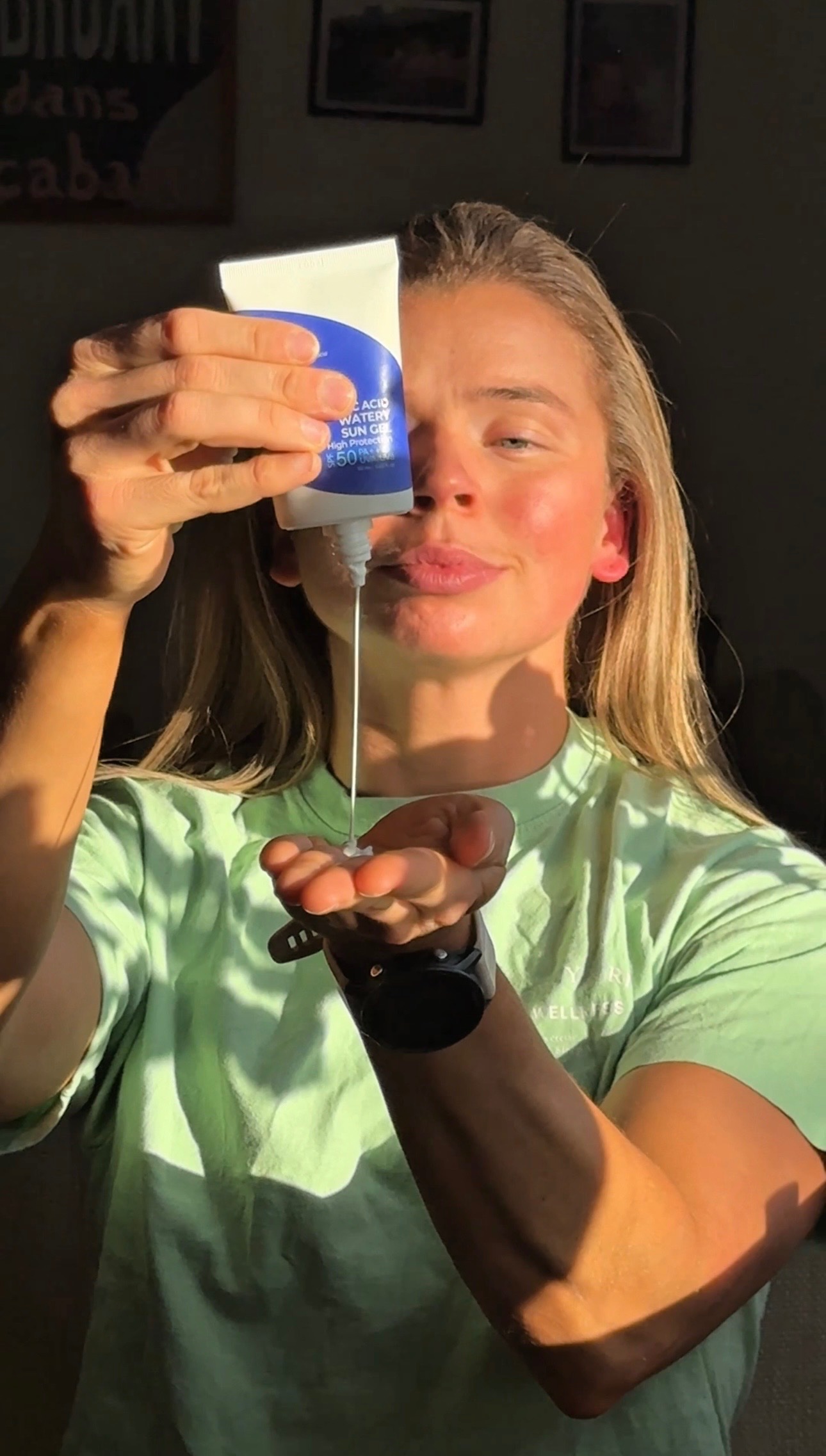 A person with long hair holds a tube of lotion above their palm, with sunlight casting a dramatic shadow.
