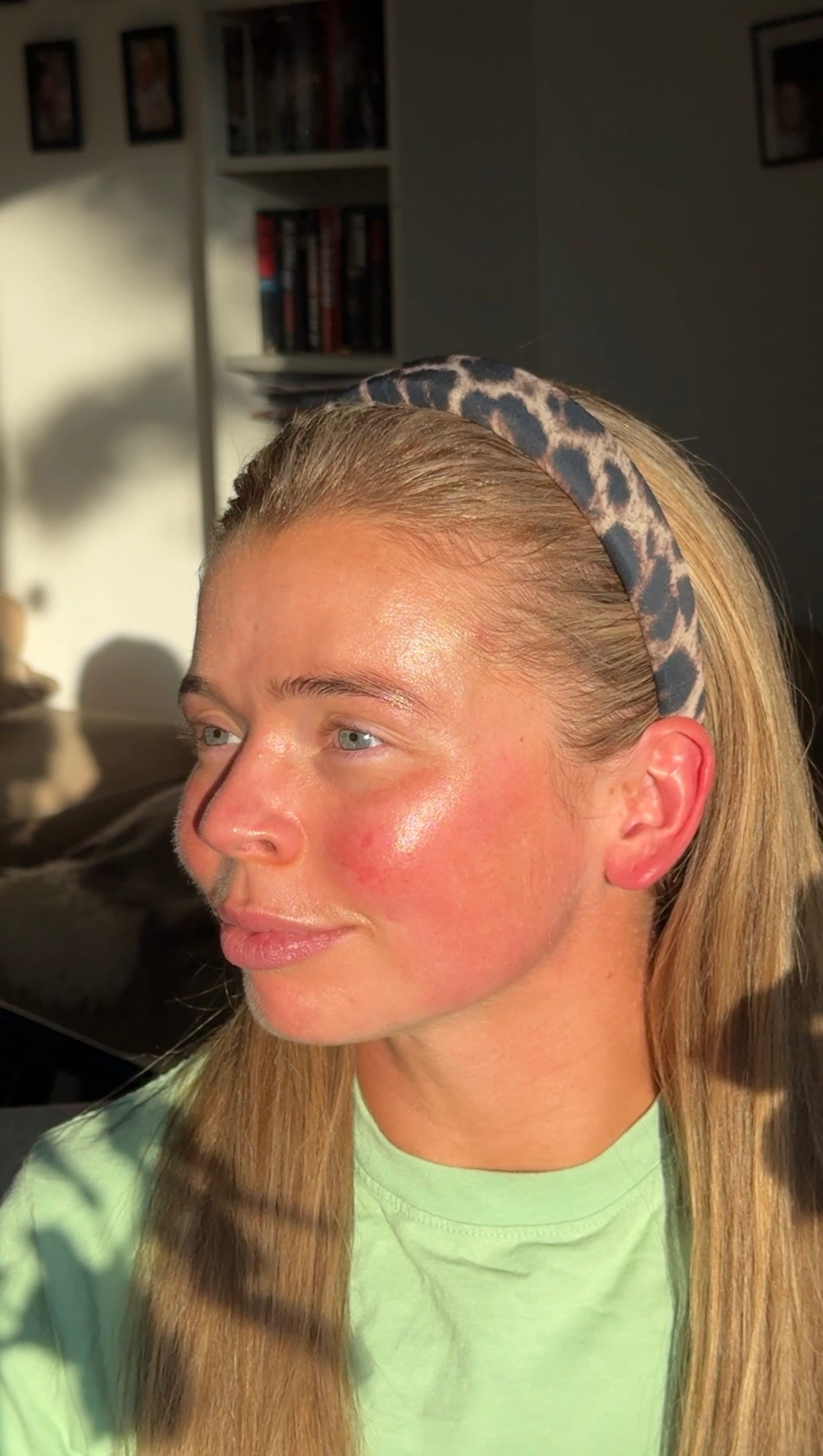 A young woman with long blonde hair and a leopard print headband is sitting in a sunlit room, showcasing a natural glow on her skin.