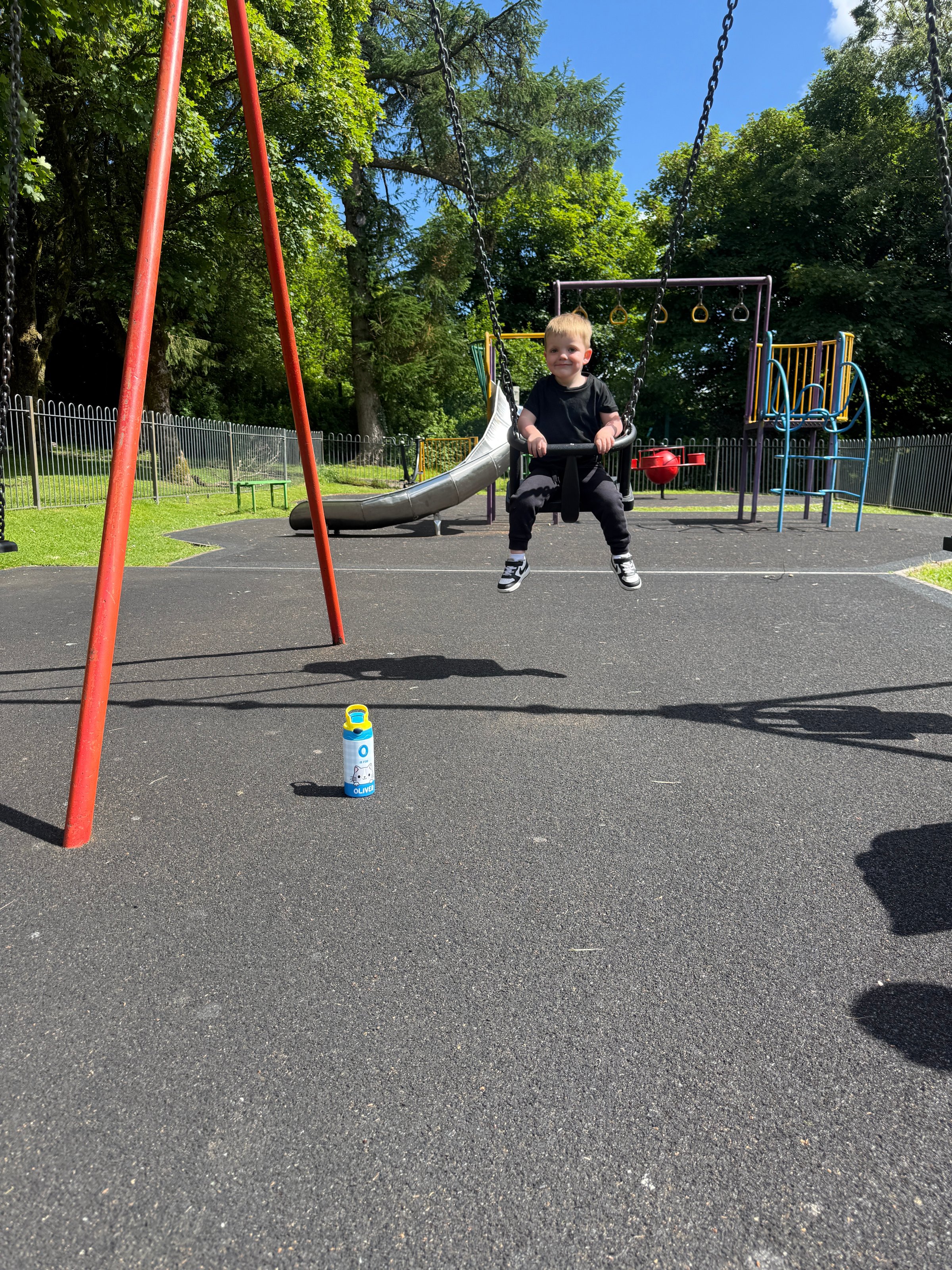 A child swings joyfully in a playground, with a can placed on the ground nearby.