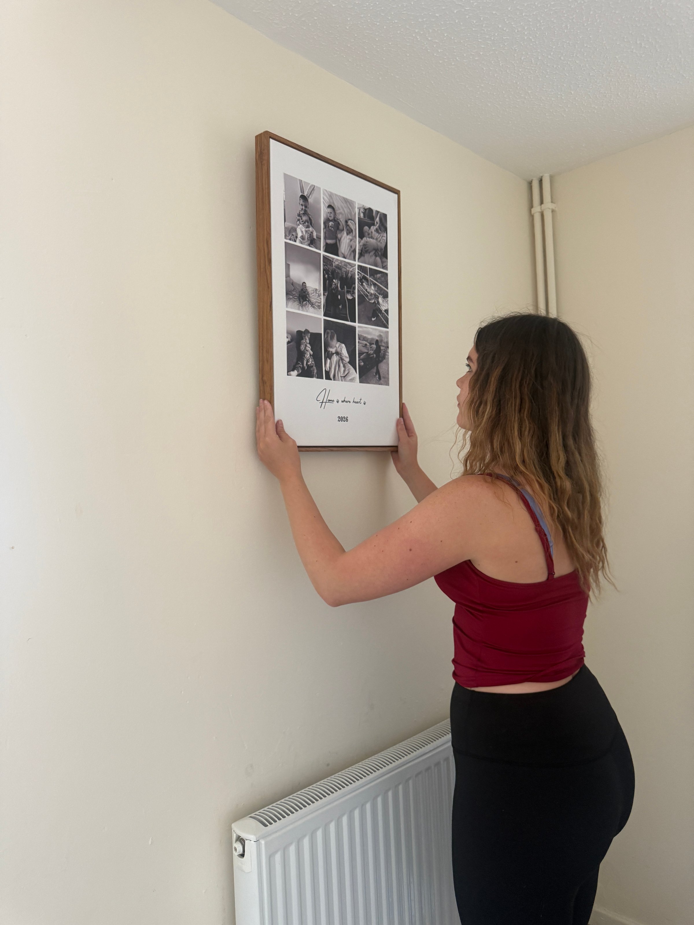 A person is hanging a framed collage of black and white photos on a wall.