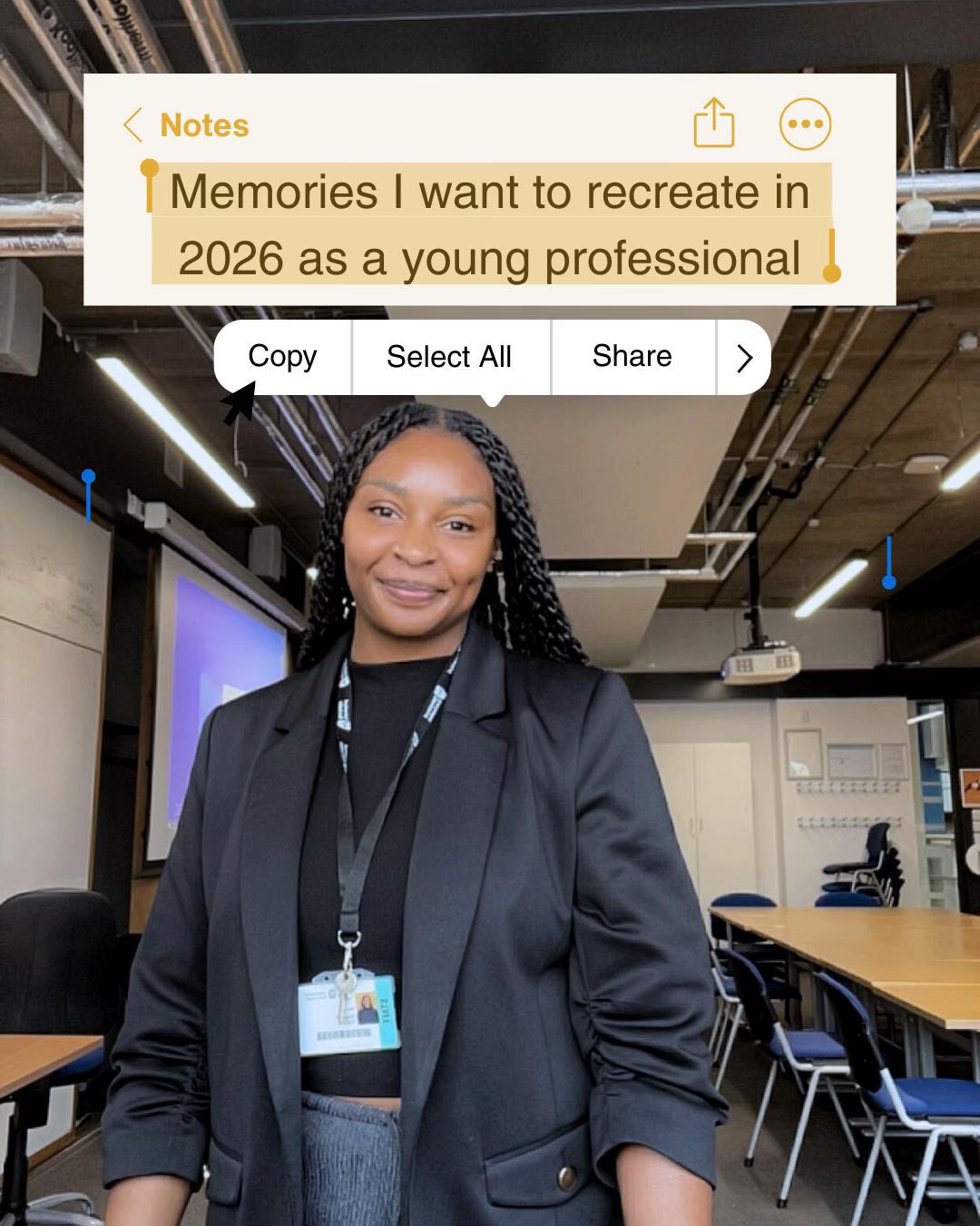 A young professional stands confidently in a modern office setting, wearing a black blazer and a name badge. The background features a classroom environment with desks and a projector.