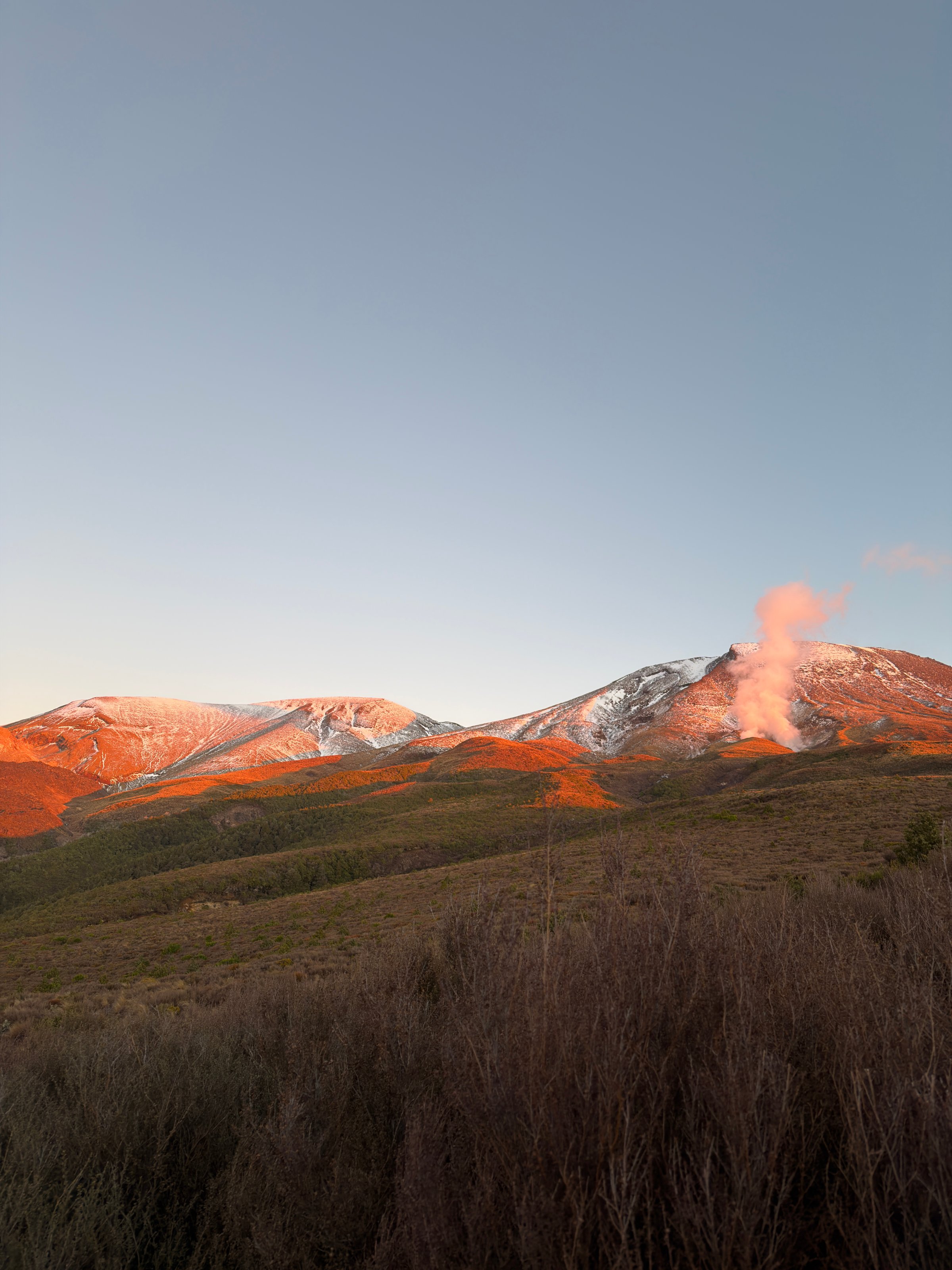 A scenic view of snow-capped mountains under a clear sky, with steam rising from the landscape in the foreground.