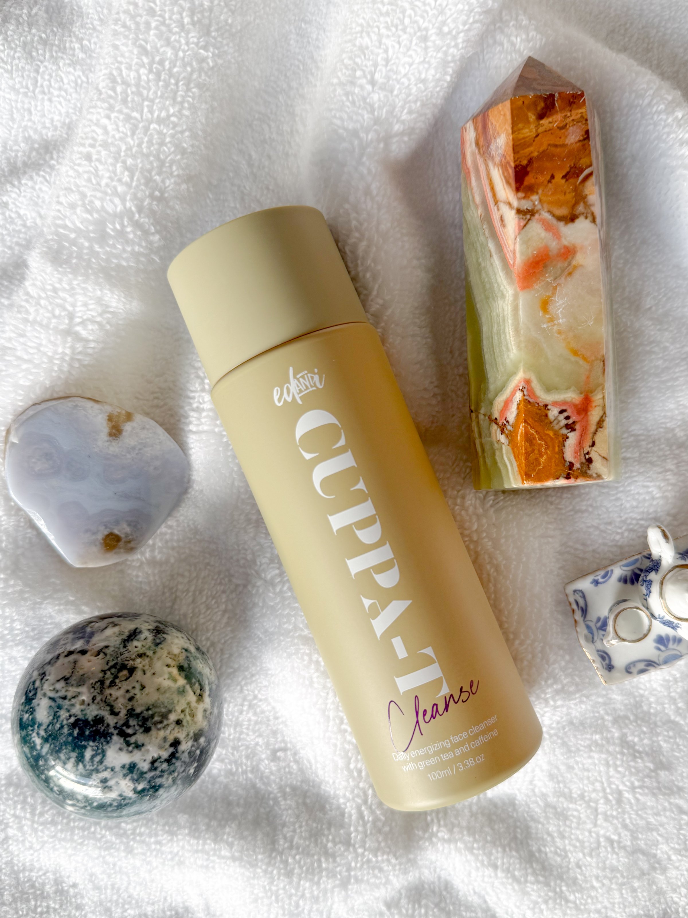 A bottle of Cupa-7 cleanse surrounded by various decorative stones and crystals on a textured white surface.
