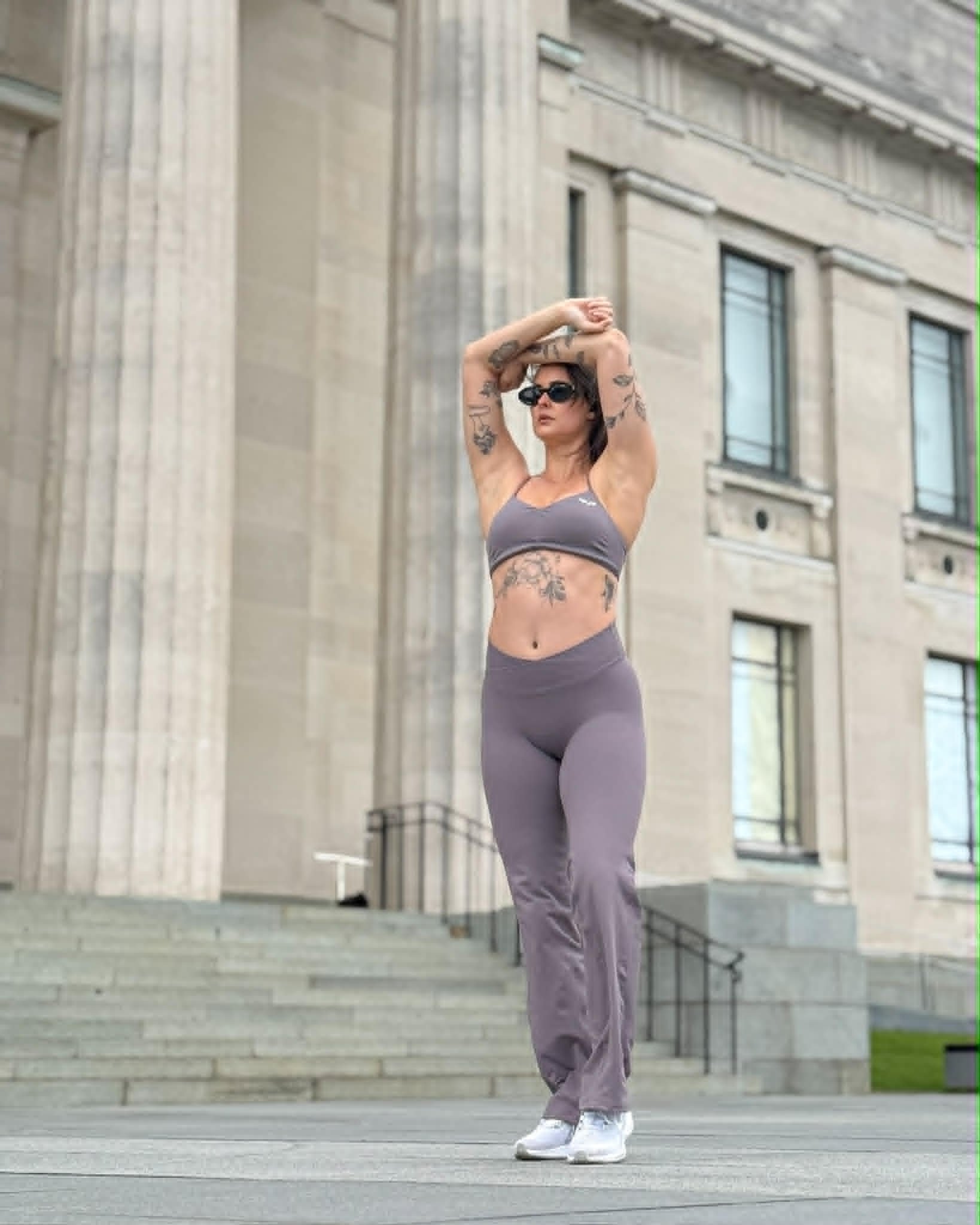 A person in athletic wear stretches outdoors in front of a large building with columns.