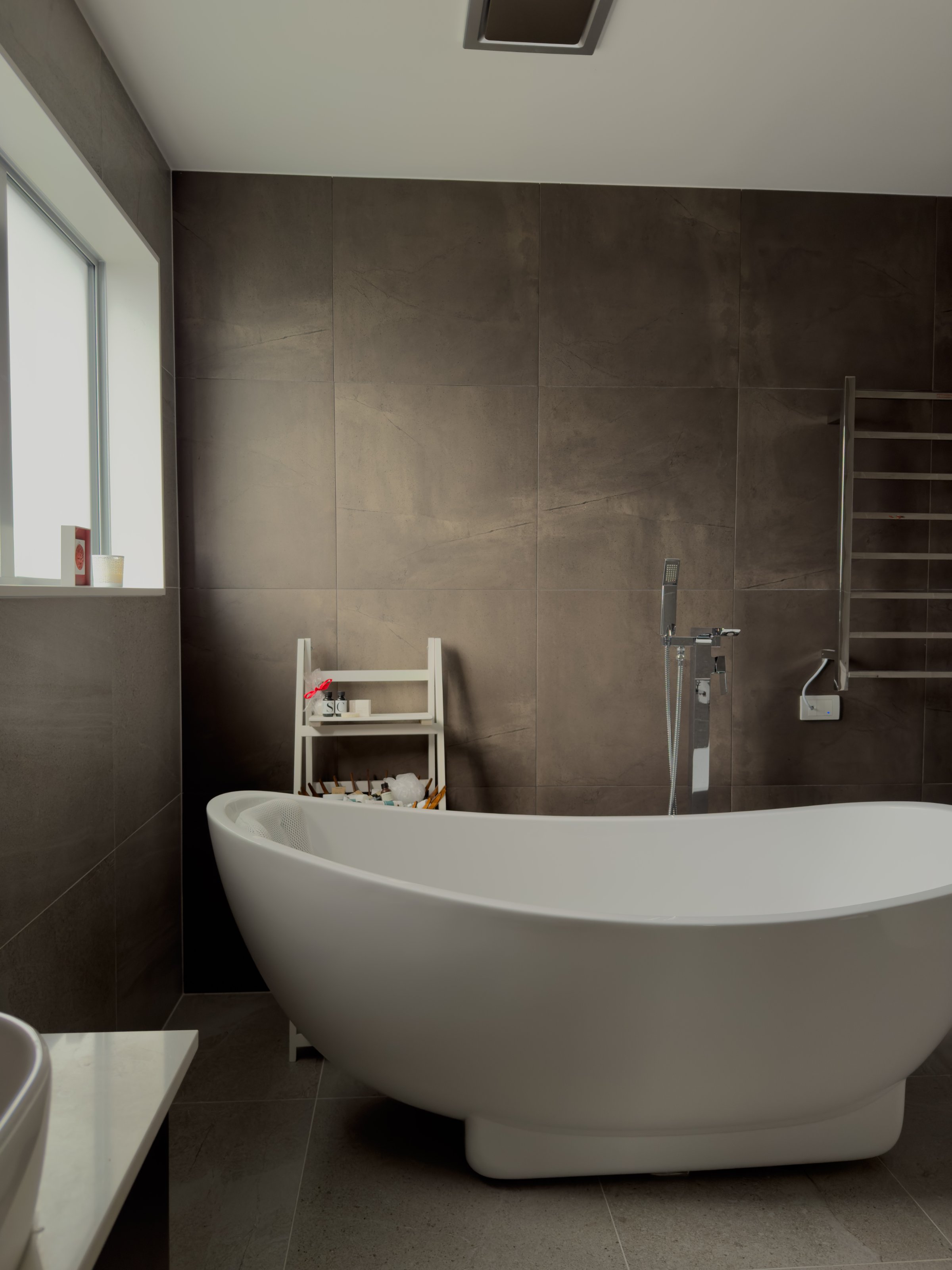 A modern bathroom featuring a sleek white bathtub and a minimalist design with dark tiled walls.