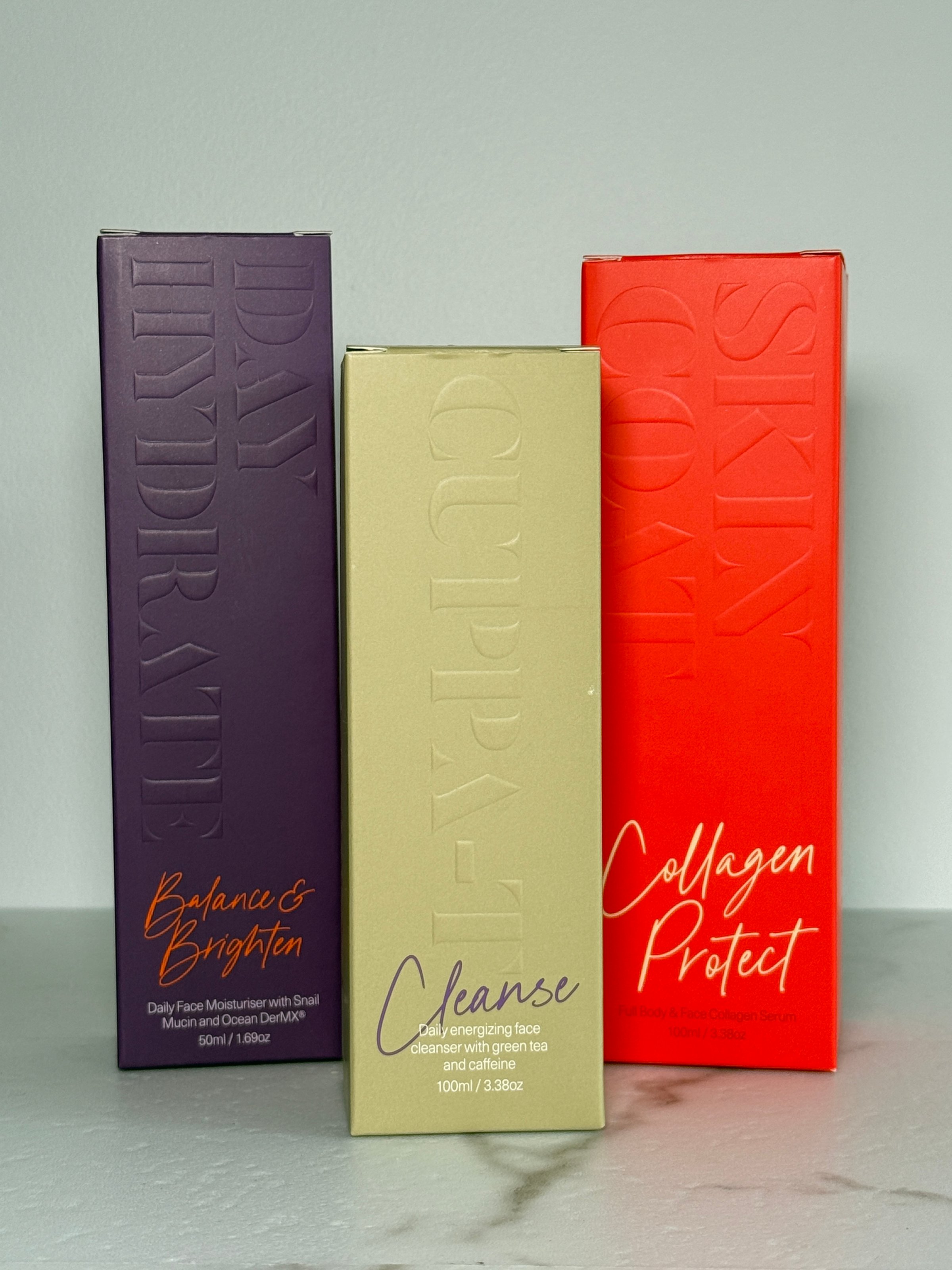 Three skincare product boxes displayed upright on a marble surface, featuring vibrant colors and distinct branding.