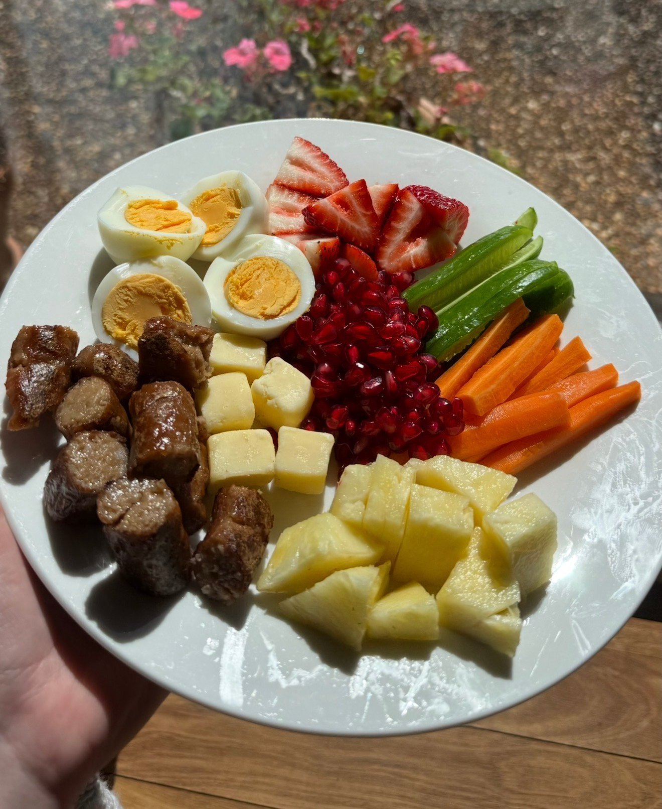 A colorful plate of assorted fruits and vegetables including boiled eggs, strawberries, celery, carrots, pomegranate seeds, and various types of melon.