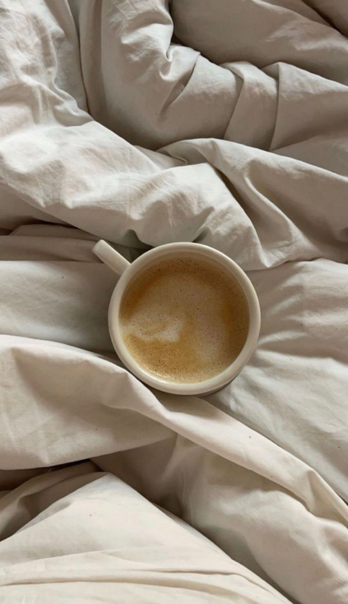 A cozy scene featuring a cup of coffee resting on a rumpled white bedspread.
