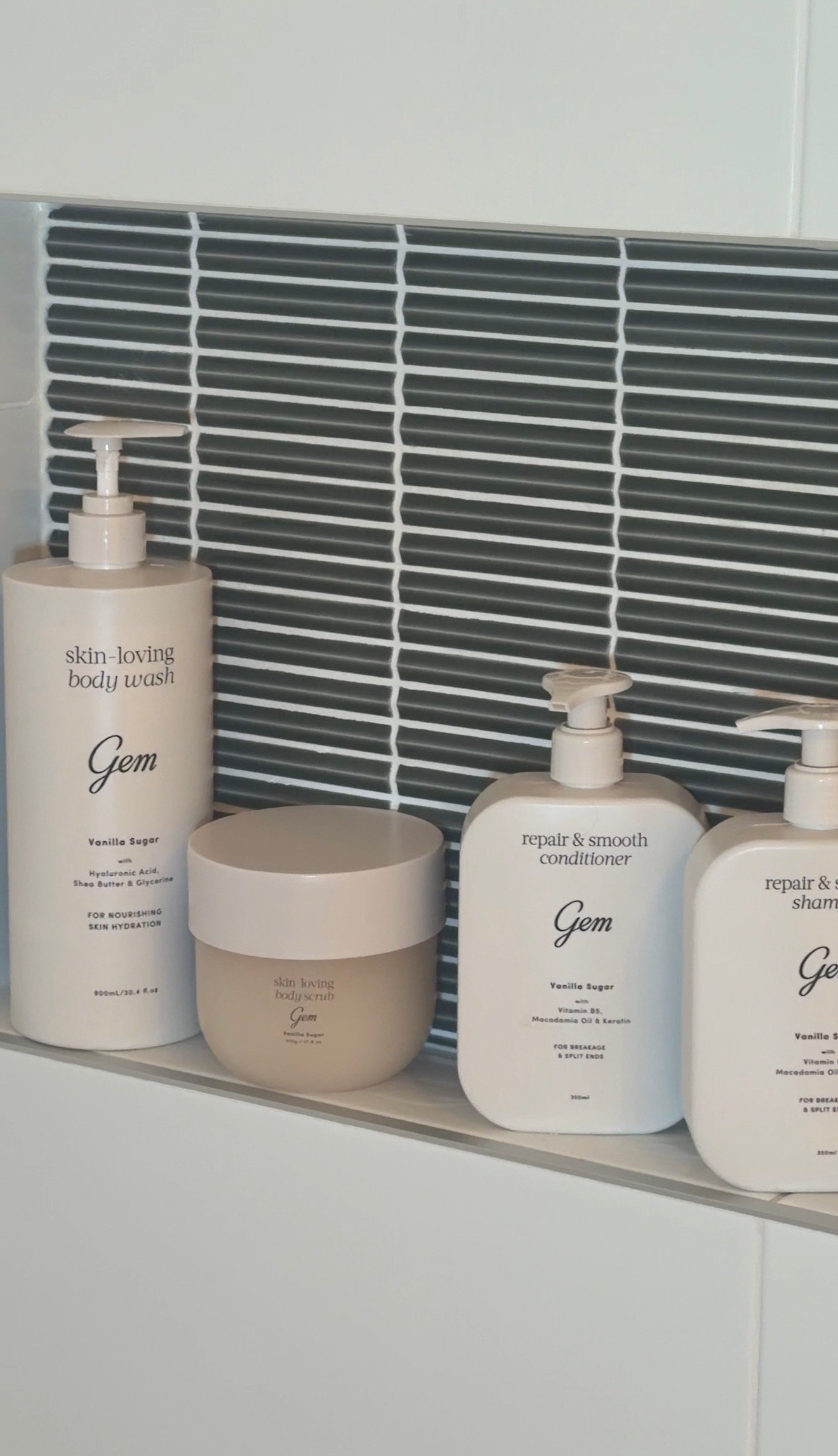 A collection of skincare products displayed on a shelf, featuring body wash, conditioner, and shampoo in minimalist packaging.